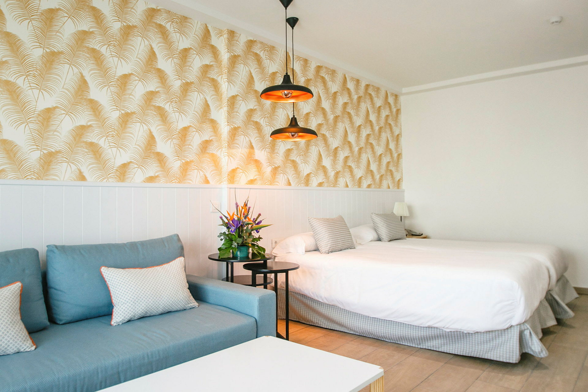 Hotellrum med blå soffa, dubbelsäng och dekorativ tapet. (AI-genererad text)