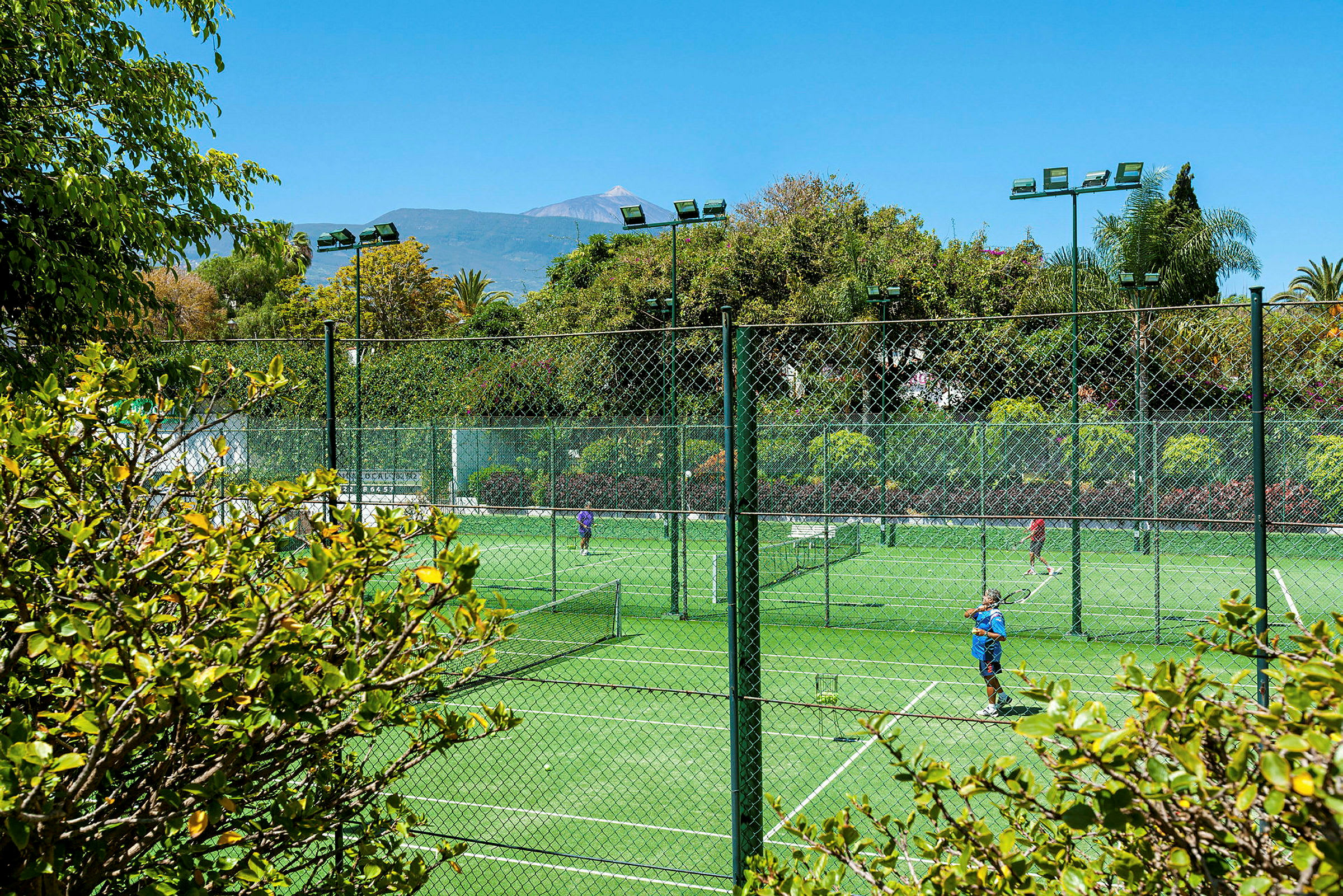 Tennisbanor utomhus omgivna av grönska och träd. (AI-genererad text)