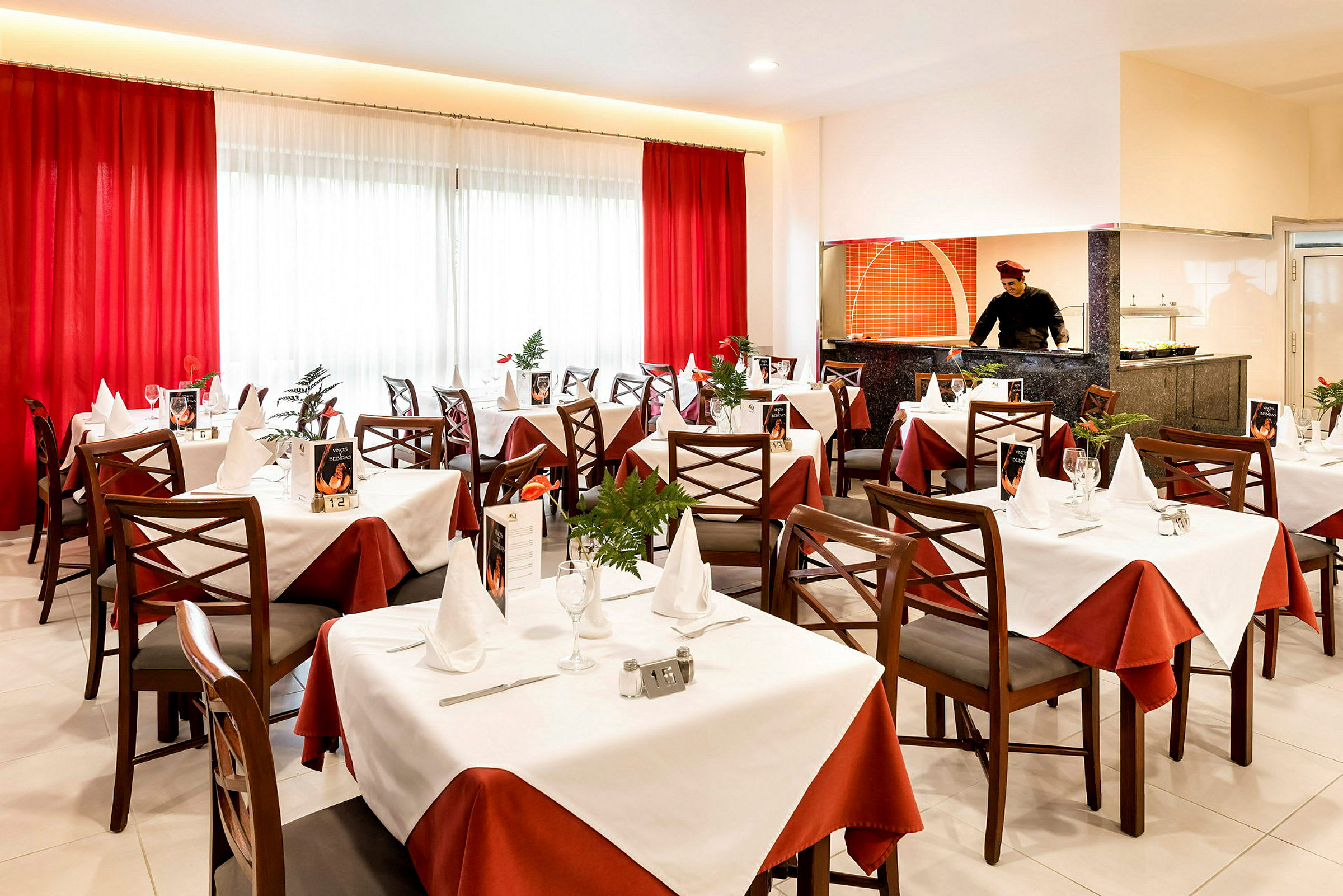 Elegant restaurang med dukade bord, vita och röda dukar och en öppen köksplats. (AI-genererad text)