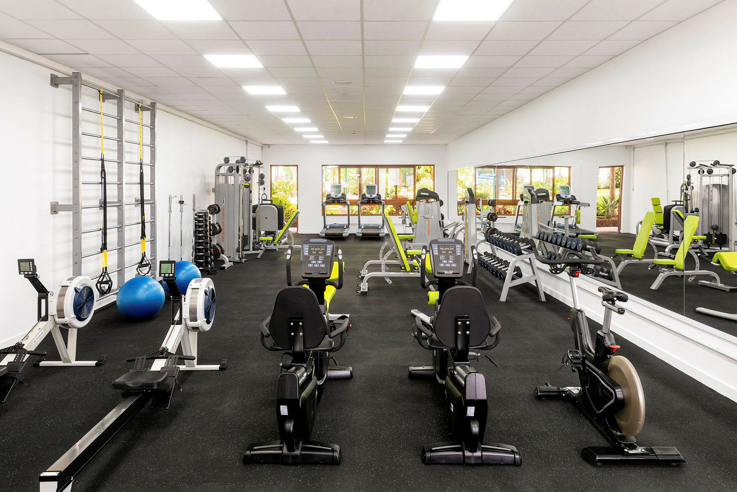 Ett gym med träningsmaskiner, speglar längs väggen och ljus inredning. (AI-genererad text)