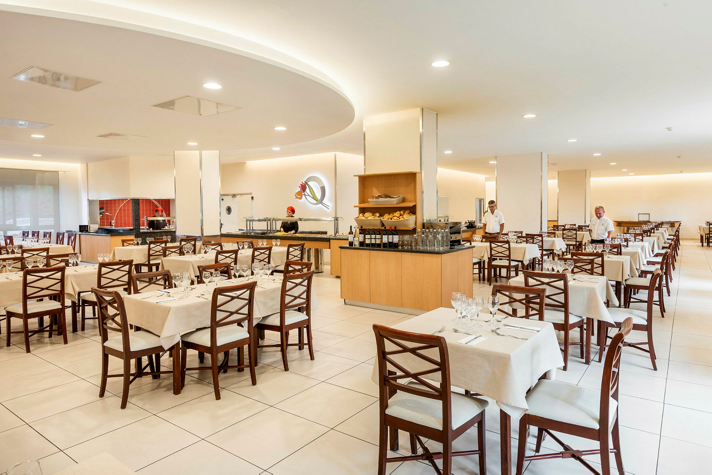 En restaurang interiör med dukade bord och stolar. Servitörer står i lokalen. (AI-genererad text)