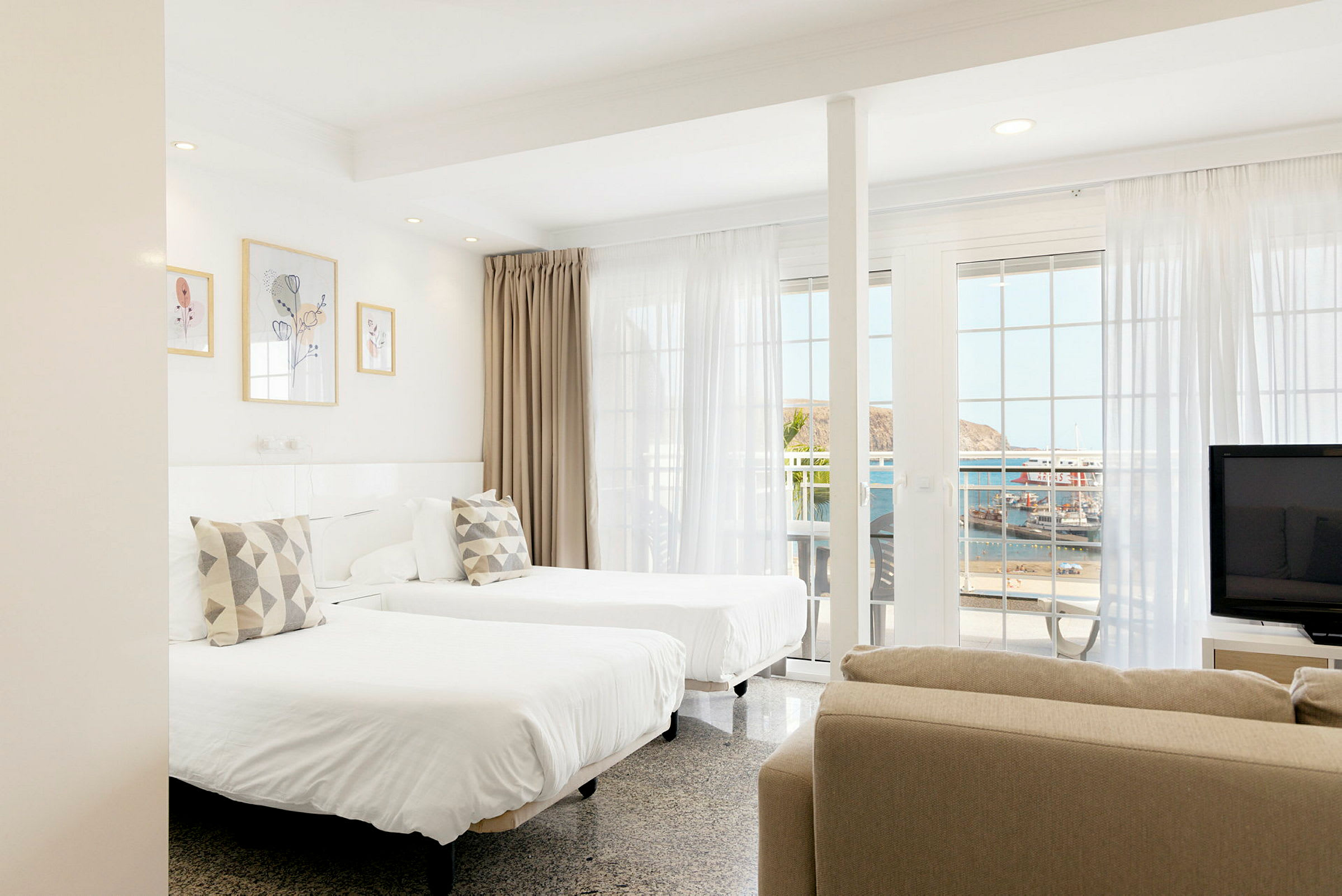 Ett ljust hotellrum med två enkelsängar, stora fönster och havsutsikt. (AI-genererad text)