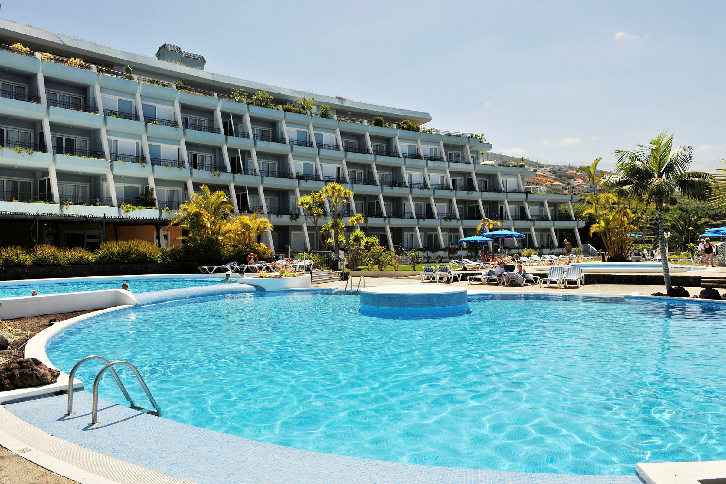 Bild av hotellbyggnad med flera våningar, pool och solstolar i förgrunden. (AI-genererad text)