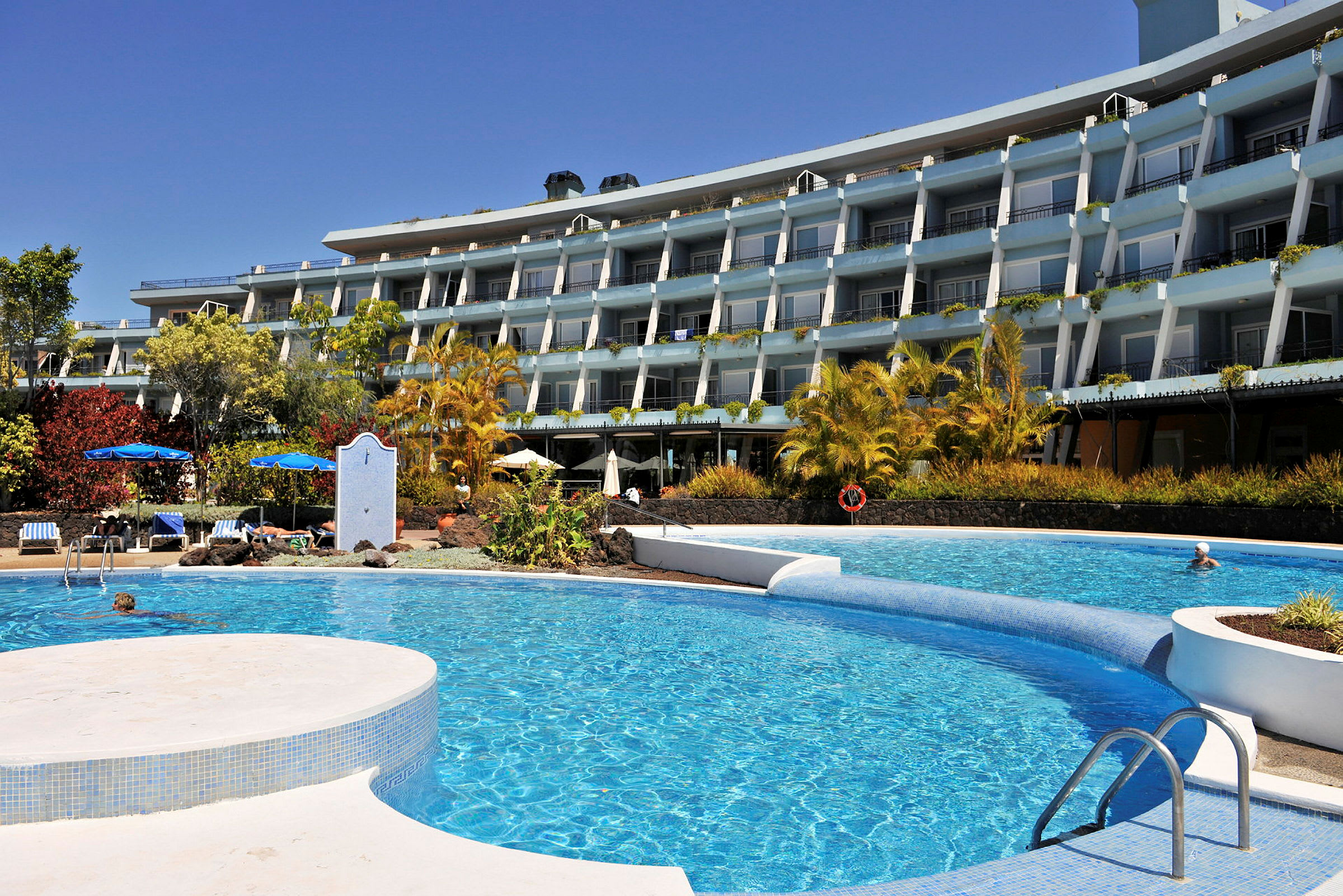 Ett hotell med flera våningar syns bakom en pool i förgrunden. (AI-genererad text)