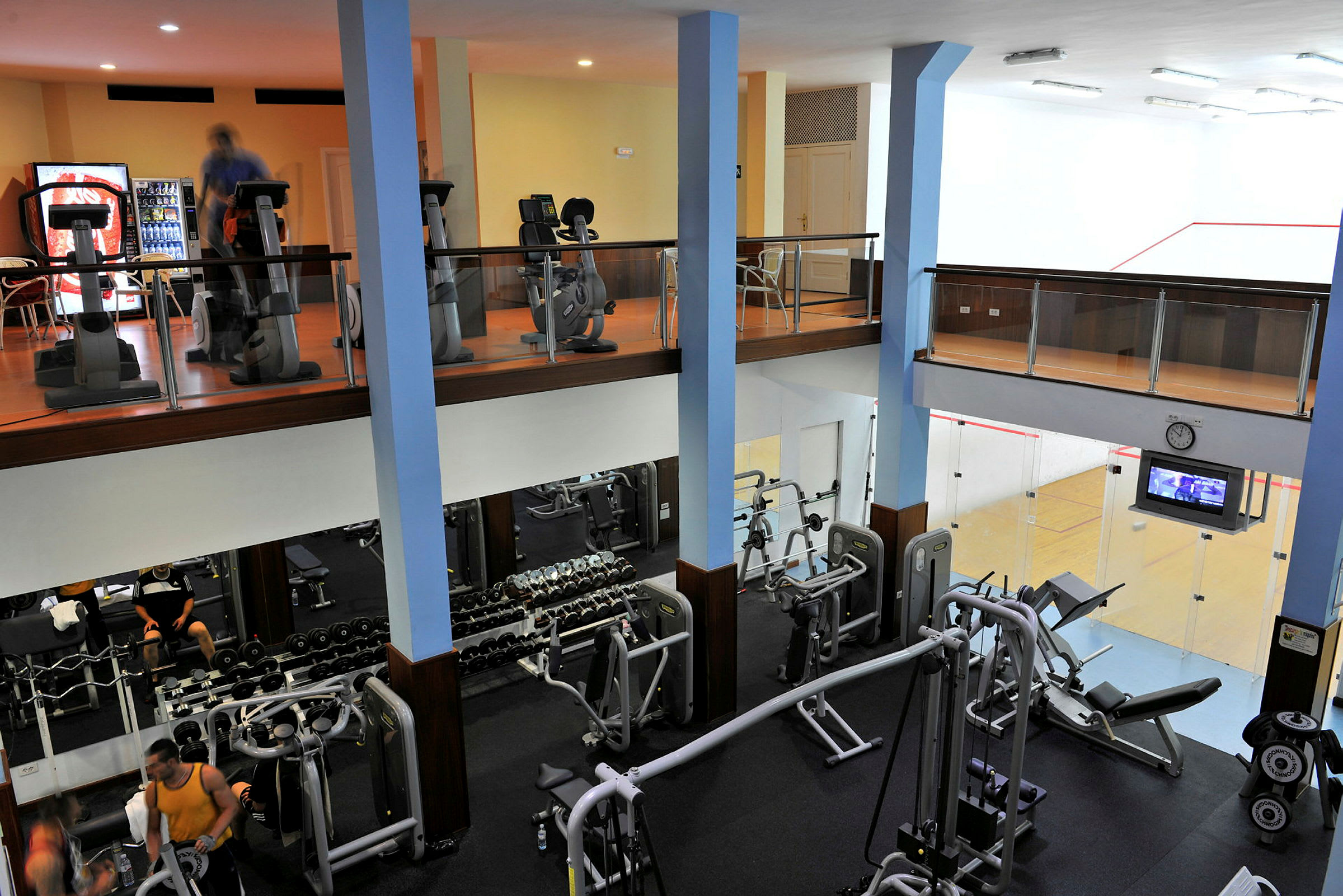 Tvåvåningsgym med träningsutrustning och en squashhall. (AI-genererad text)