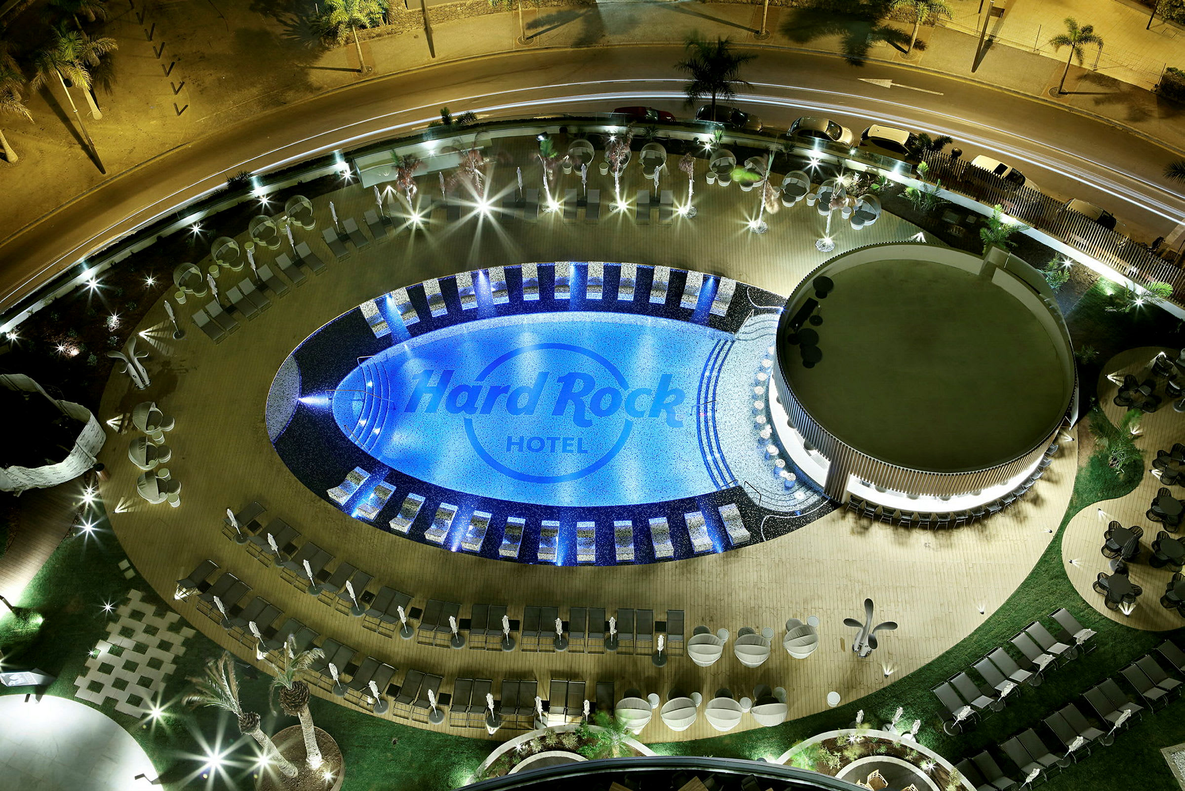 Luftvy av en upplyst pool och omgivande området vid Hard Rock Hotel under kvällstid. (AI-genererad text)