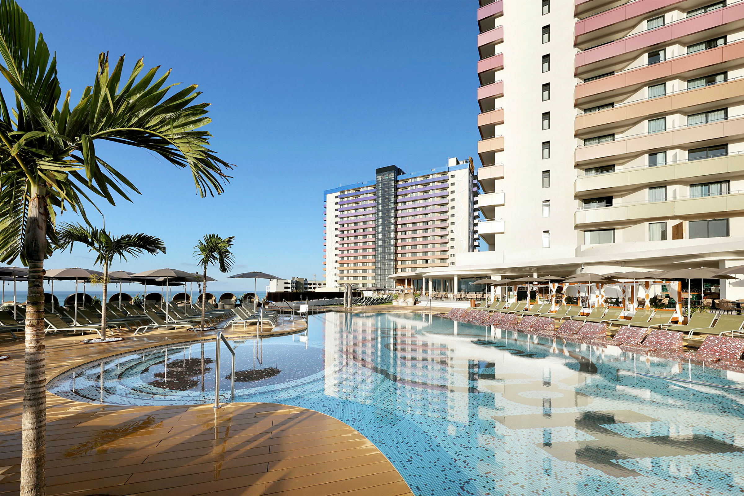 En utomhuspool vid ett hotell med palmer och solstolar. (AI-genererad text)