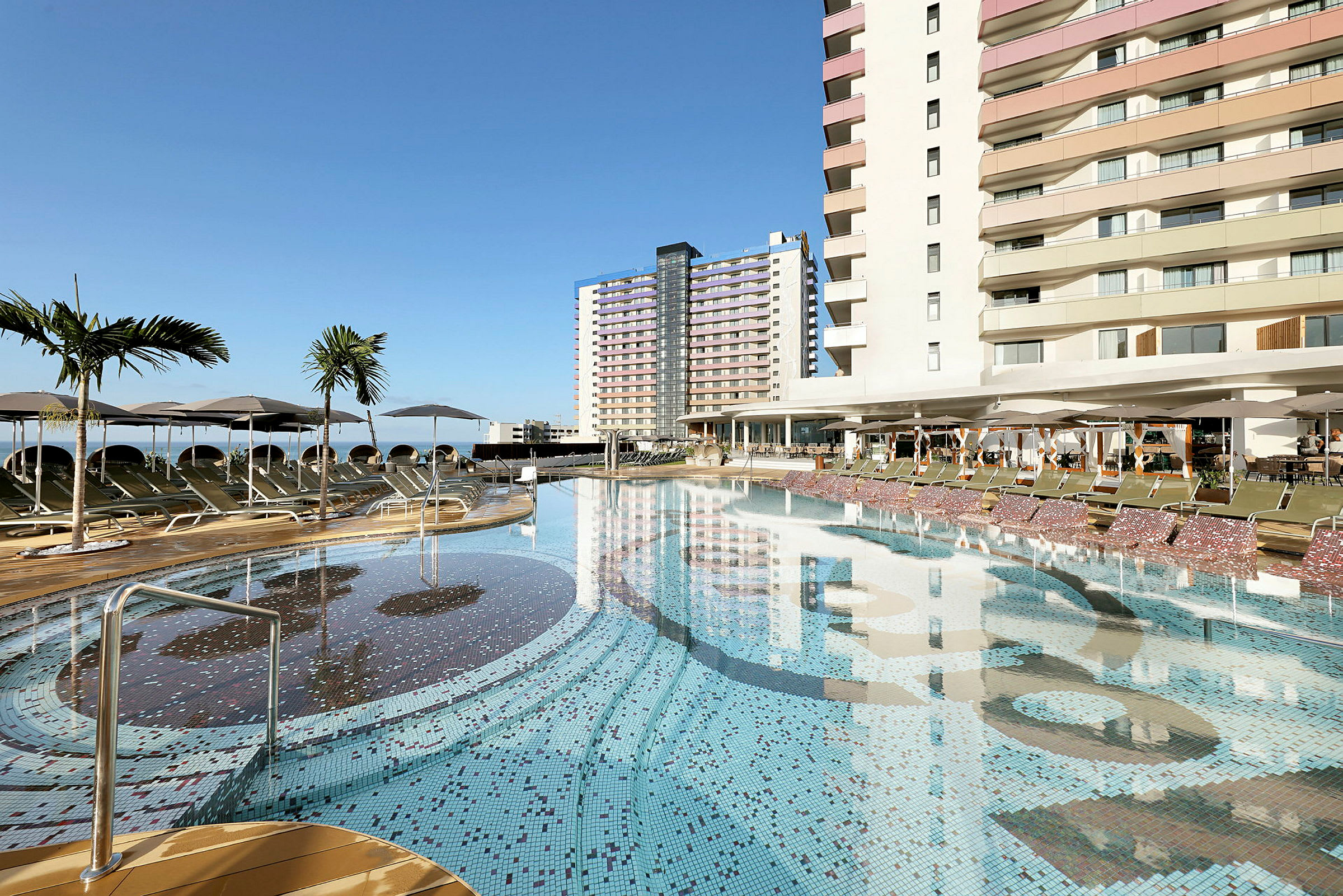 En utomhuspool vid ett hotell med solstolar och parasoller. (AI-genererad text)