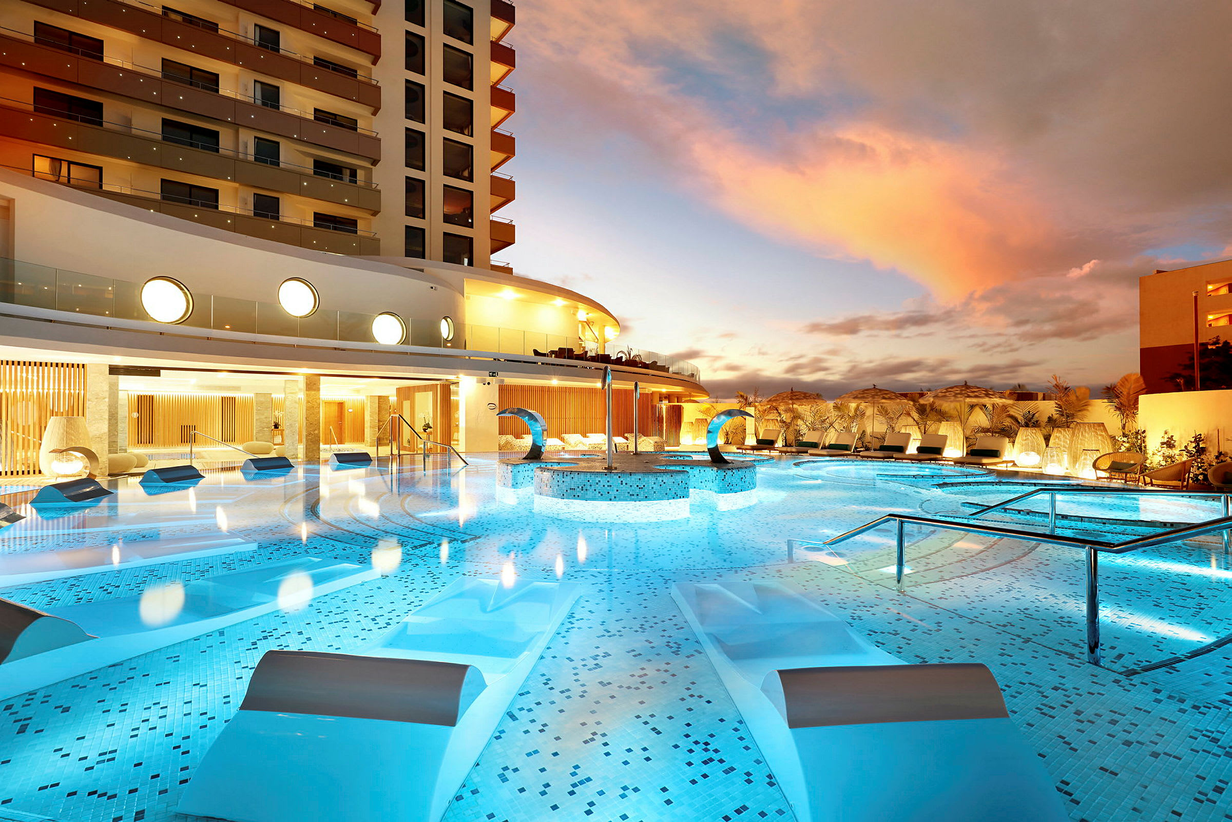 En lyxig pool i ett hotellområde med modern arkitektur och solstolar vid skymning. (AI-genererad text)