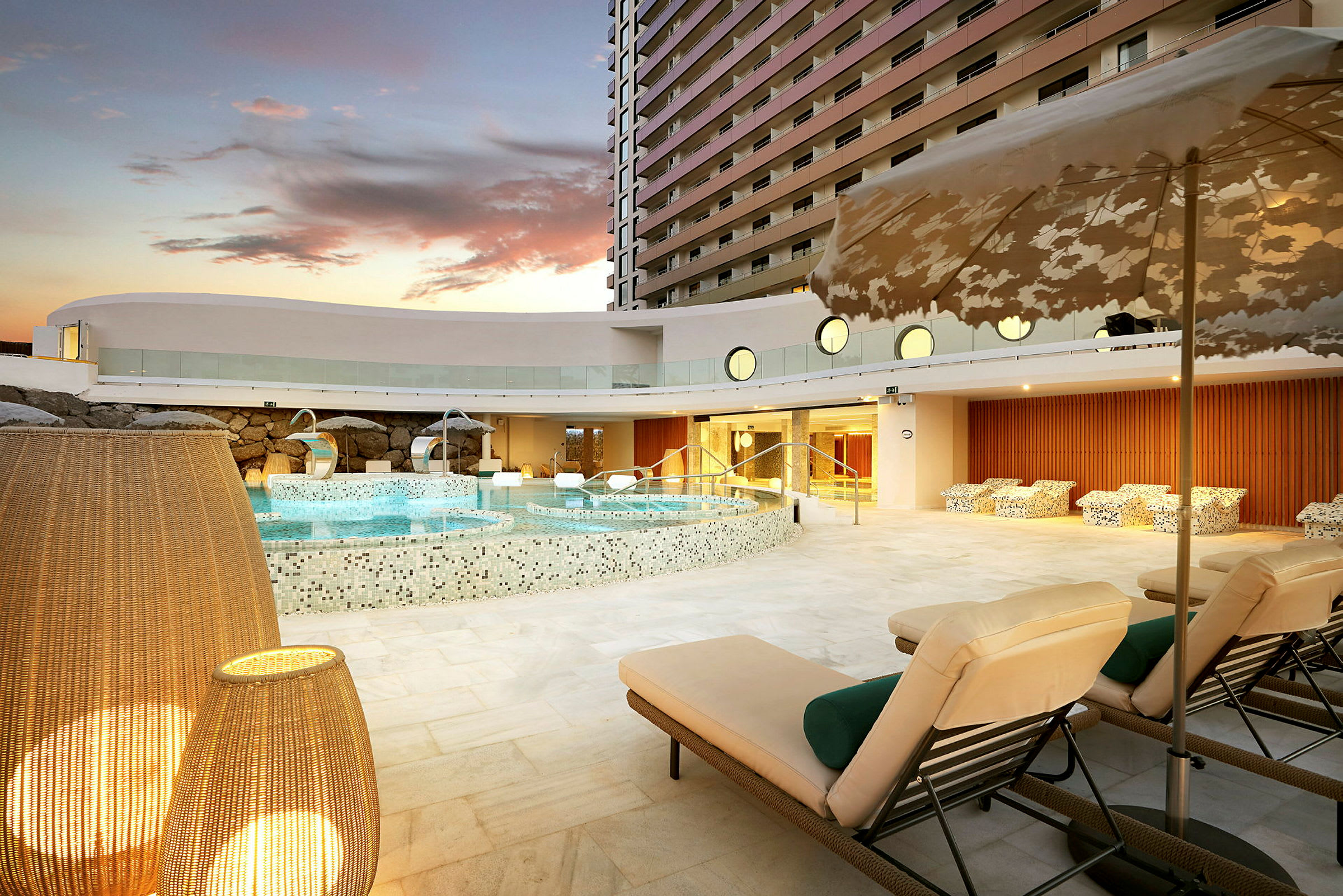 Hotellpoolområde med solstolar och dekorativa lampor i förgrunden. (AI-genererad text)