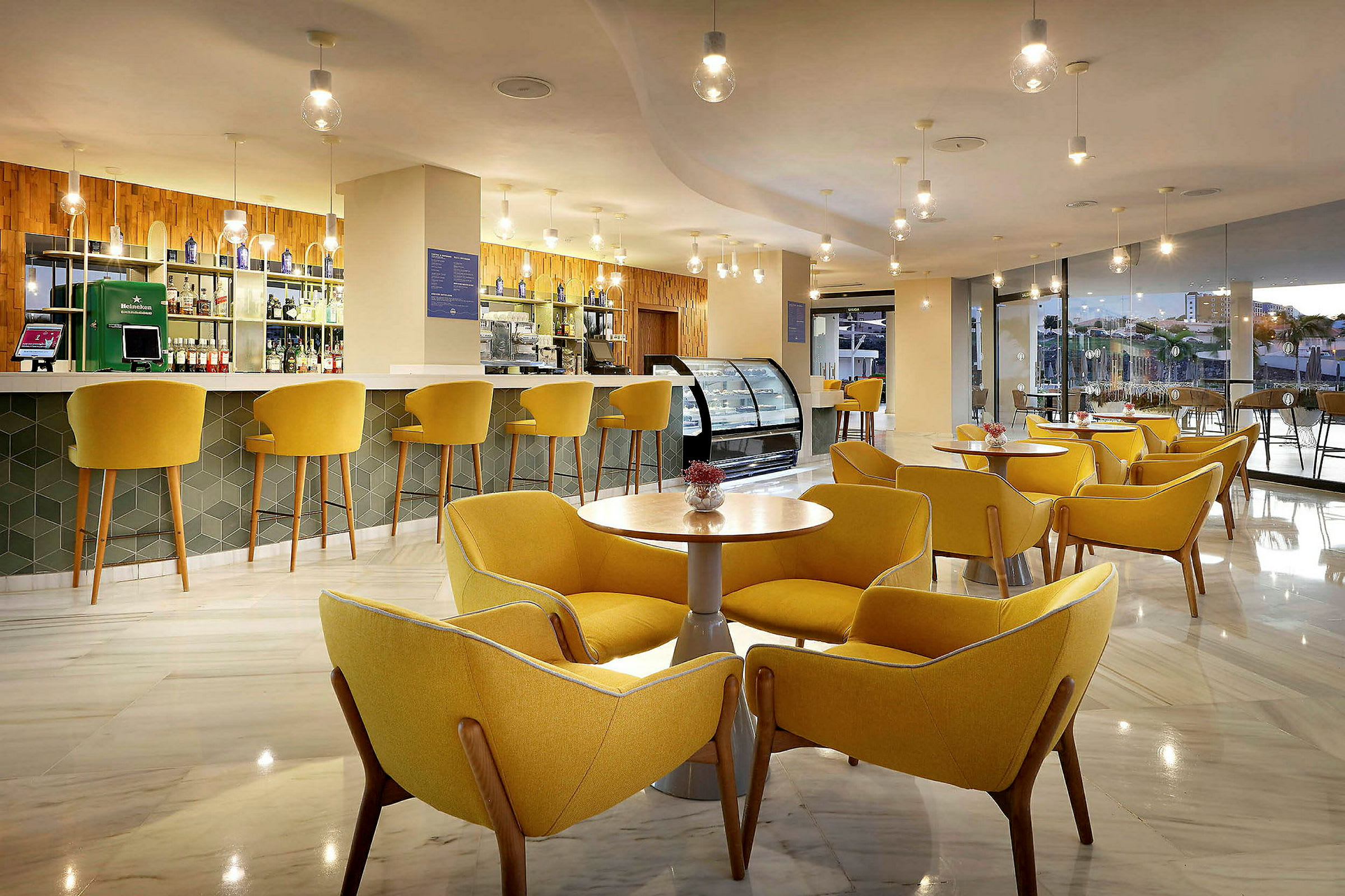En modern lounge med gula stolar och bord samt en bar i bakgrunden. (AI-genererad text)