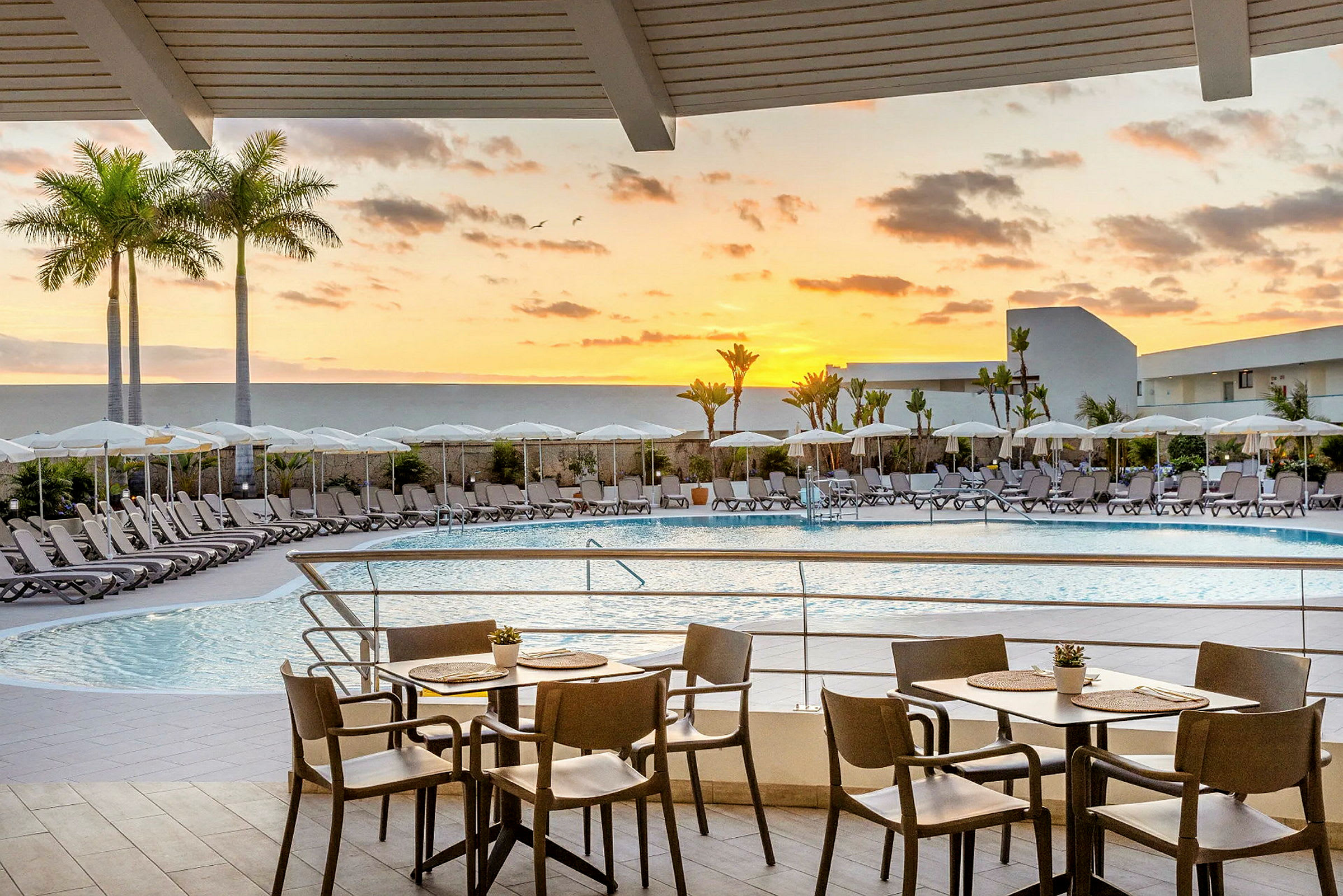 Hotellpoolområde med solstolar och parasoller vid solnedgången. (AI-genererad text)