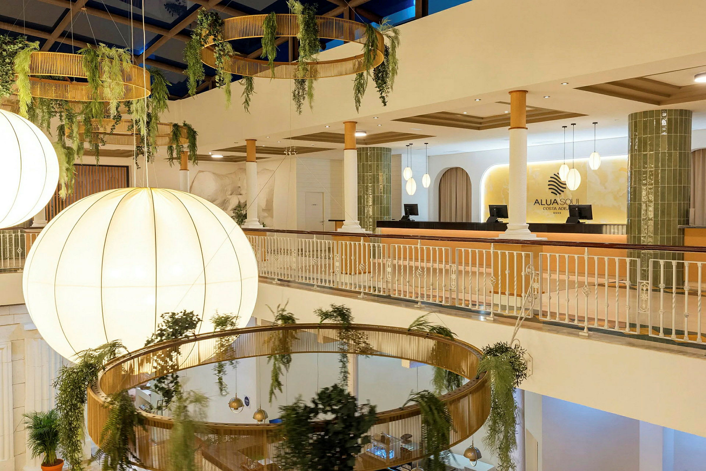 Interiör av en hotellobby med stora ljuskronor, hängande växtdekorationer och receptionen synlig. (AI-genererad text)