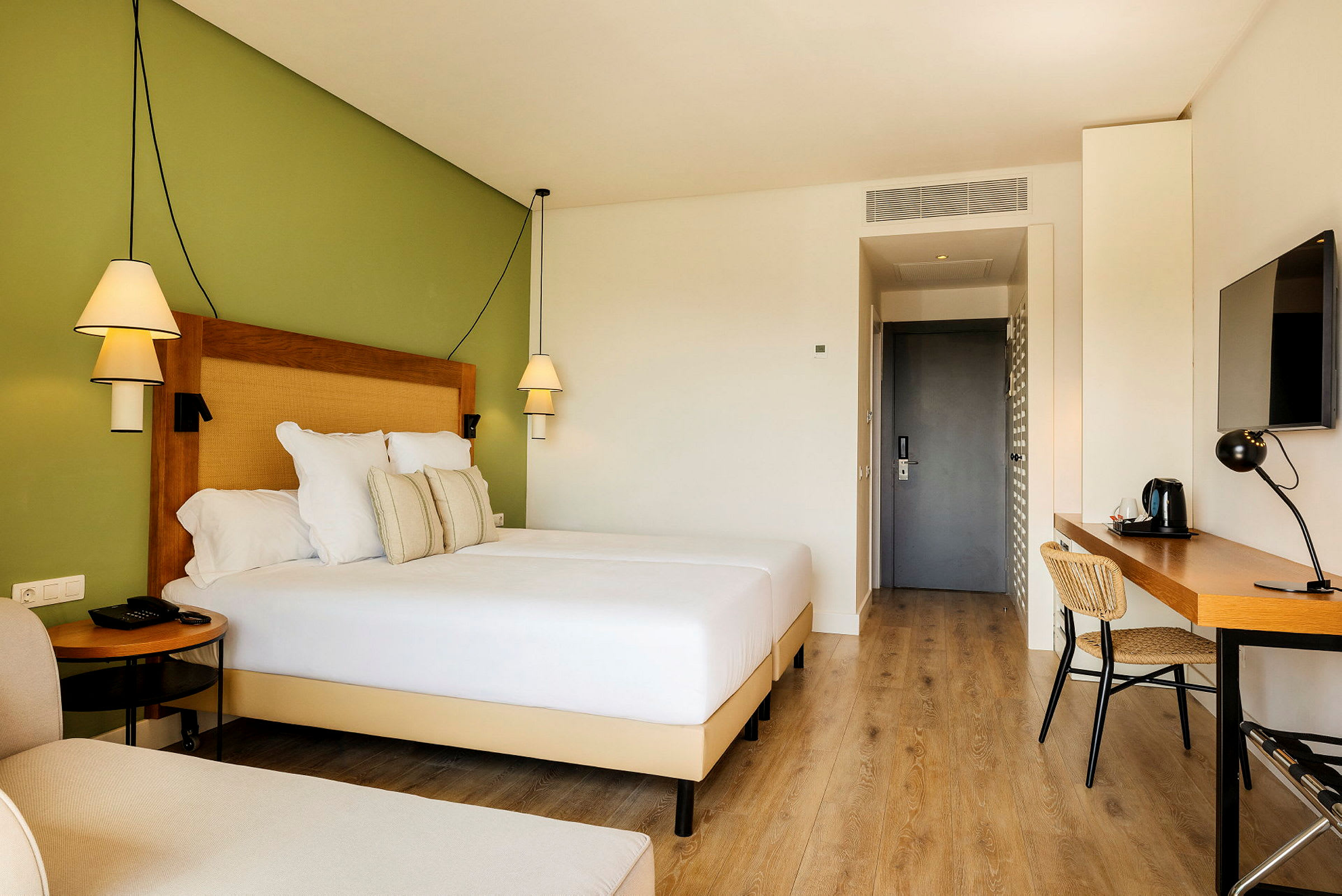 Hotellrum med en bred säng, skrivbord och grön vägg. (AI-genererad text)