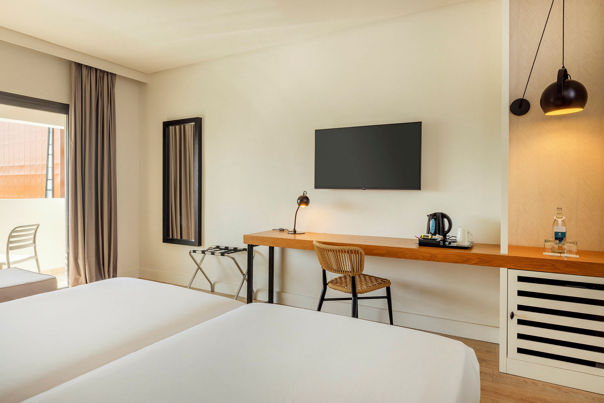 Ett hotellrum med en skrivbordsyta, en stol och en säng, samt en väggmonterad TV. (AI-genererad text)