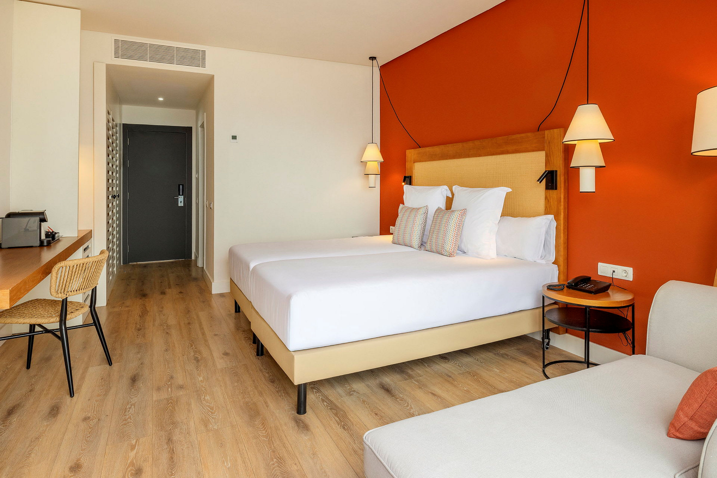 Ett hotellrum med en orange vägg, en dubbelsäng, skrivbord och stolar. (AI-genererad text)
