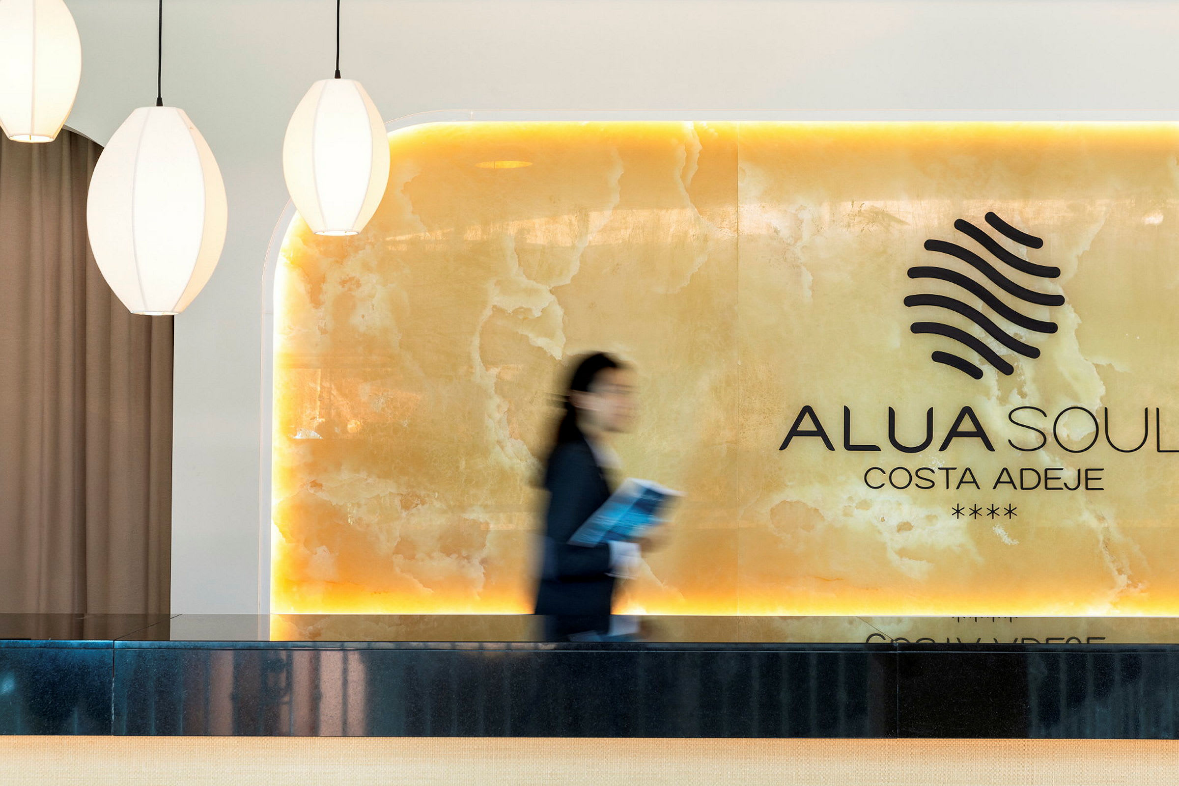 Receptionen på Alua Soul Costa Adeje visas med ljusa detaljer och en person i rörelse. (AI-genererad text)