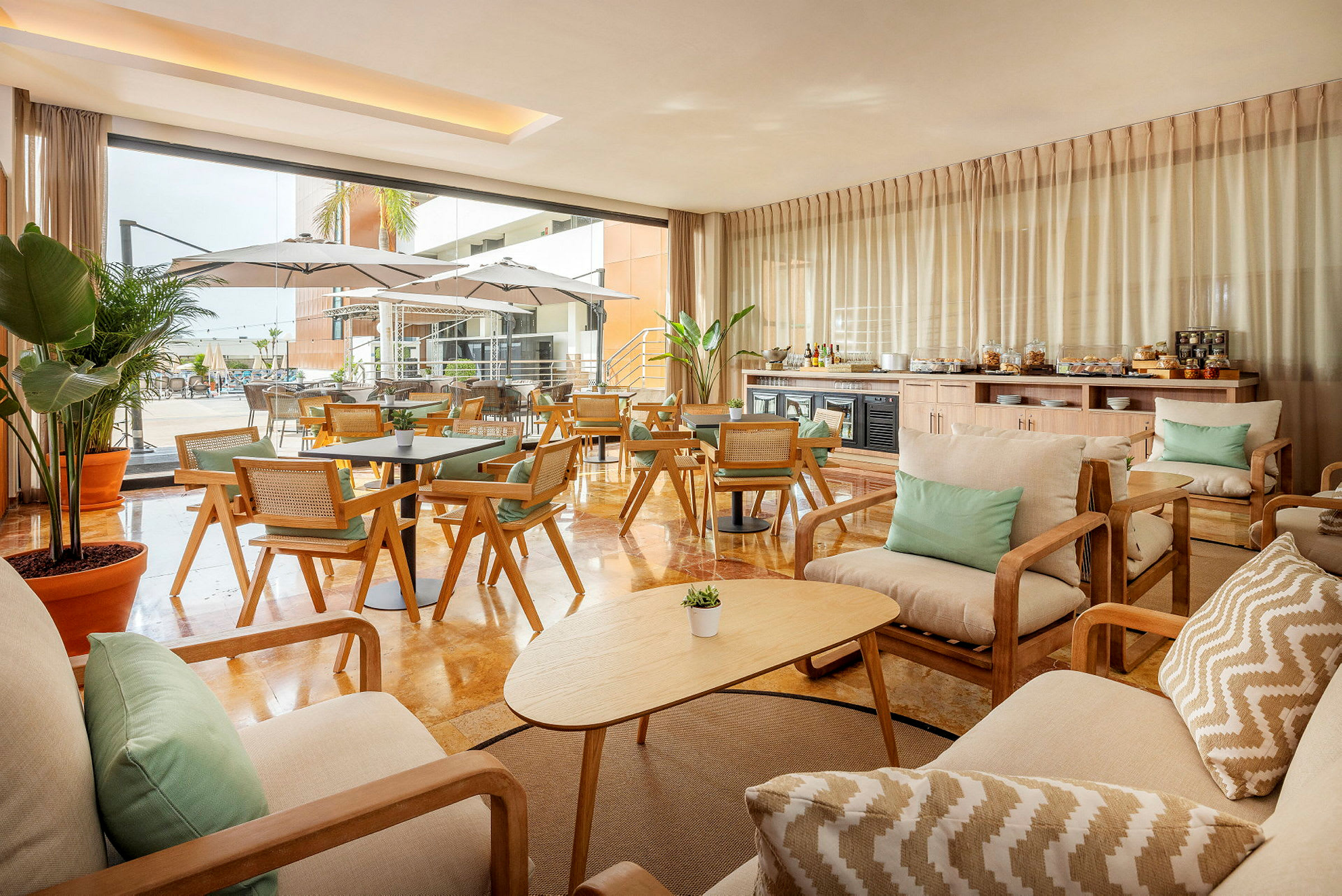 En elegant lounge med trämöbler och tygkuddar. Utsikt mot en utomhuspool med parasoller. (AI-genererad text)