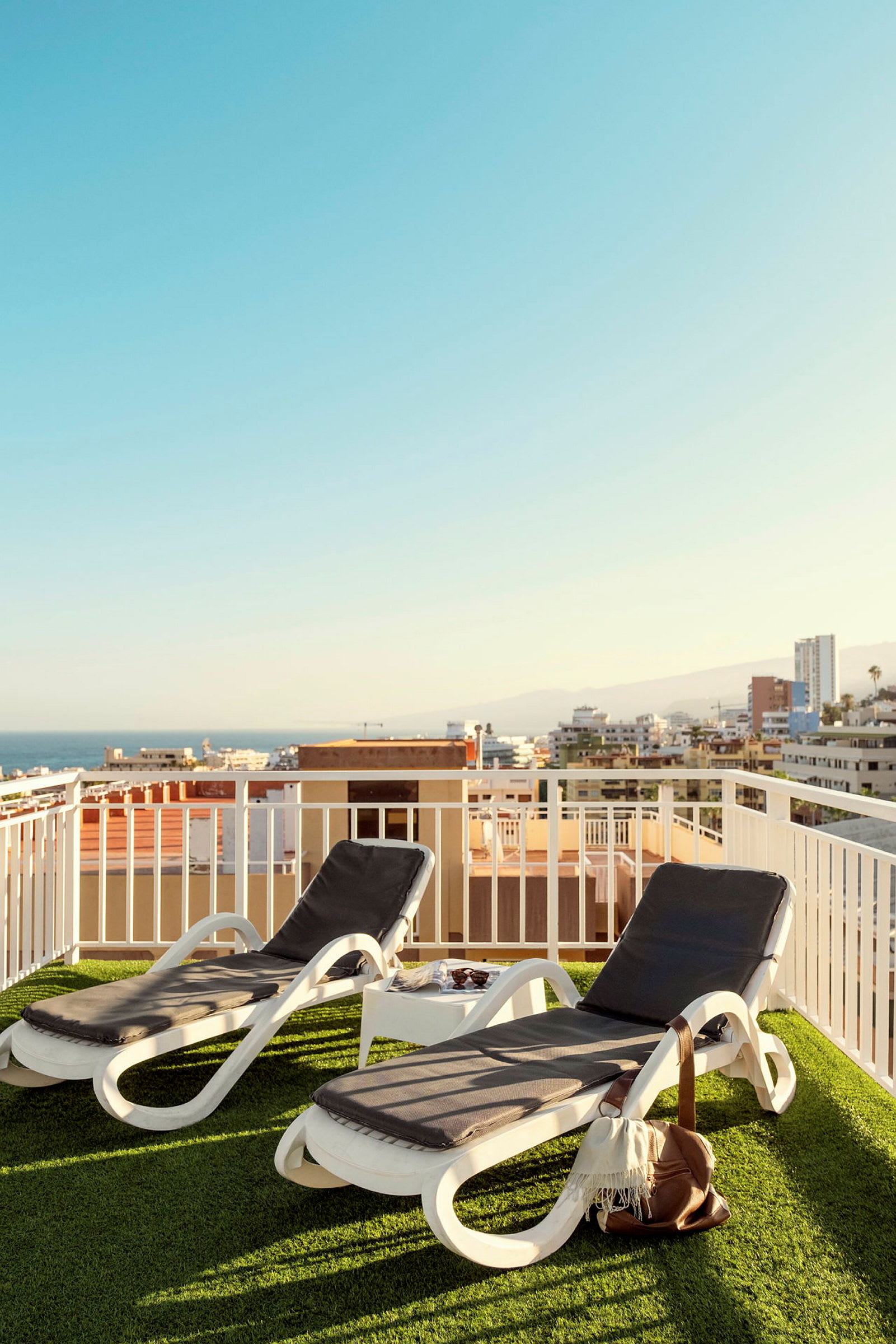 Två solstolar på en terrass med utsikt över byggnader och hav. (AI-genererad text)
