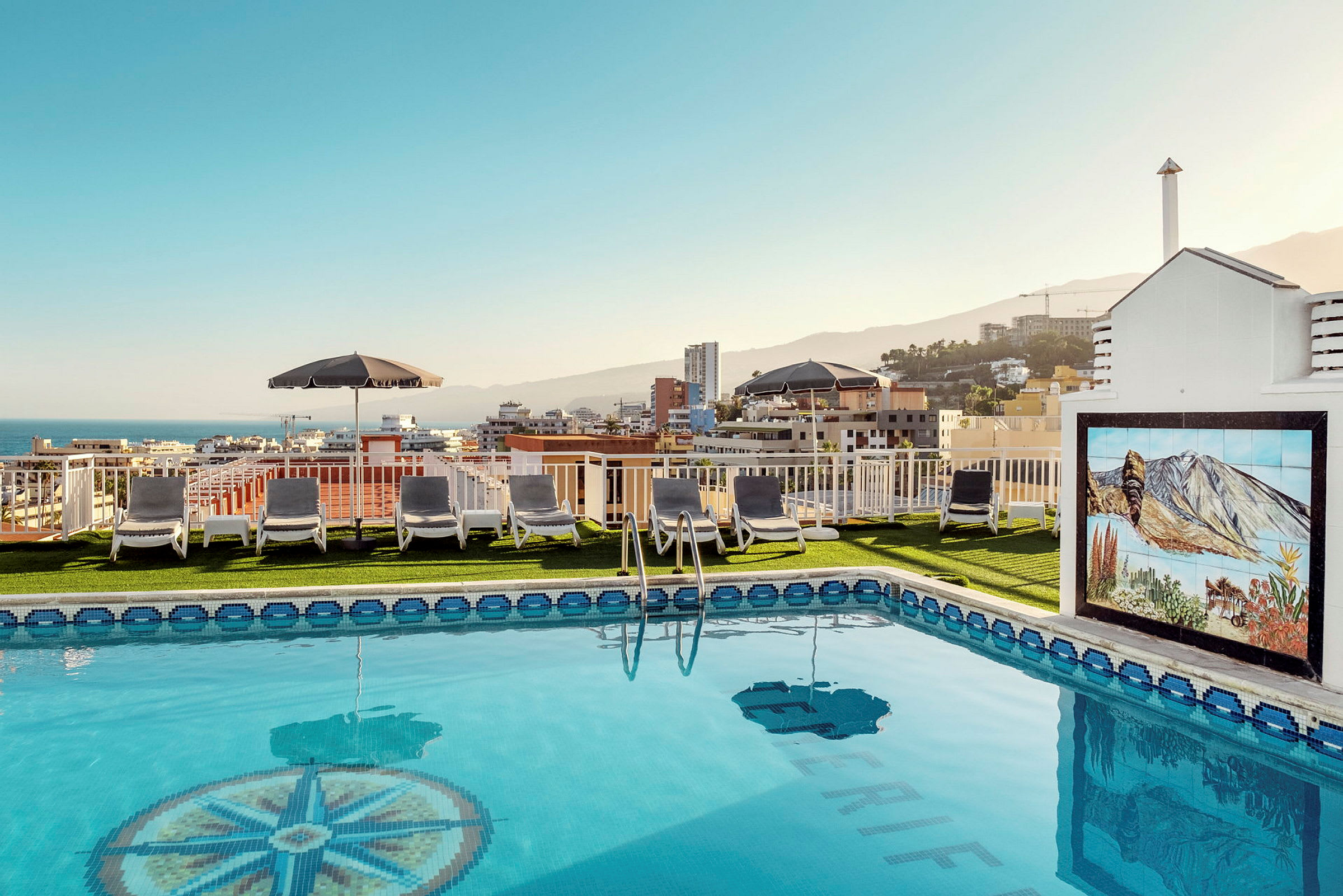 Bild av en pool med solstolar på takterrass och utsikt över en stad. (AI-genererad text)