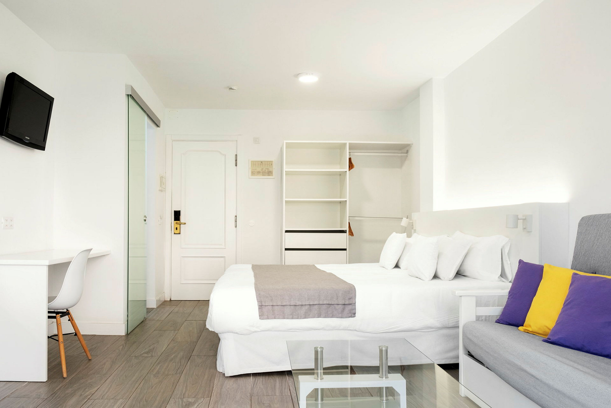Modernt hotellrum med vit inredning och färgade kuddar. (AI-genererad text)