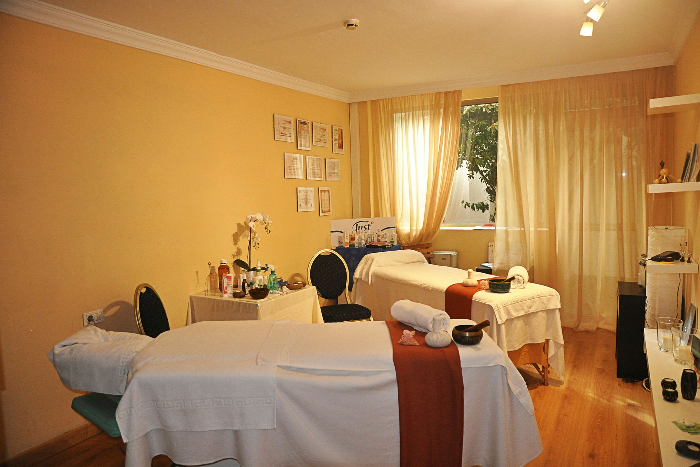 Två massagebänkar i ett varmt inrett rum med ljusgul vägg och gardiner. (AI-genererad text)