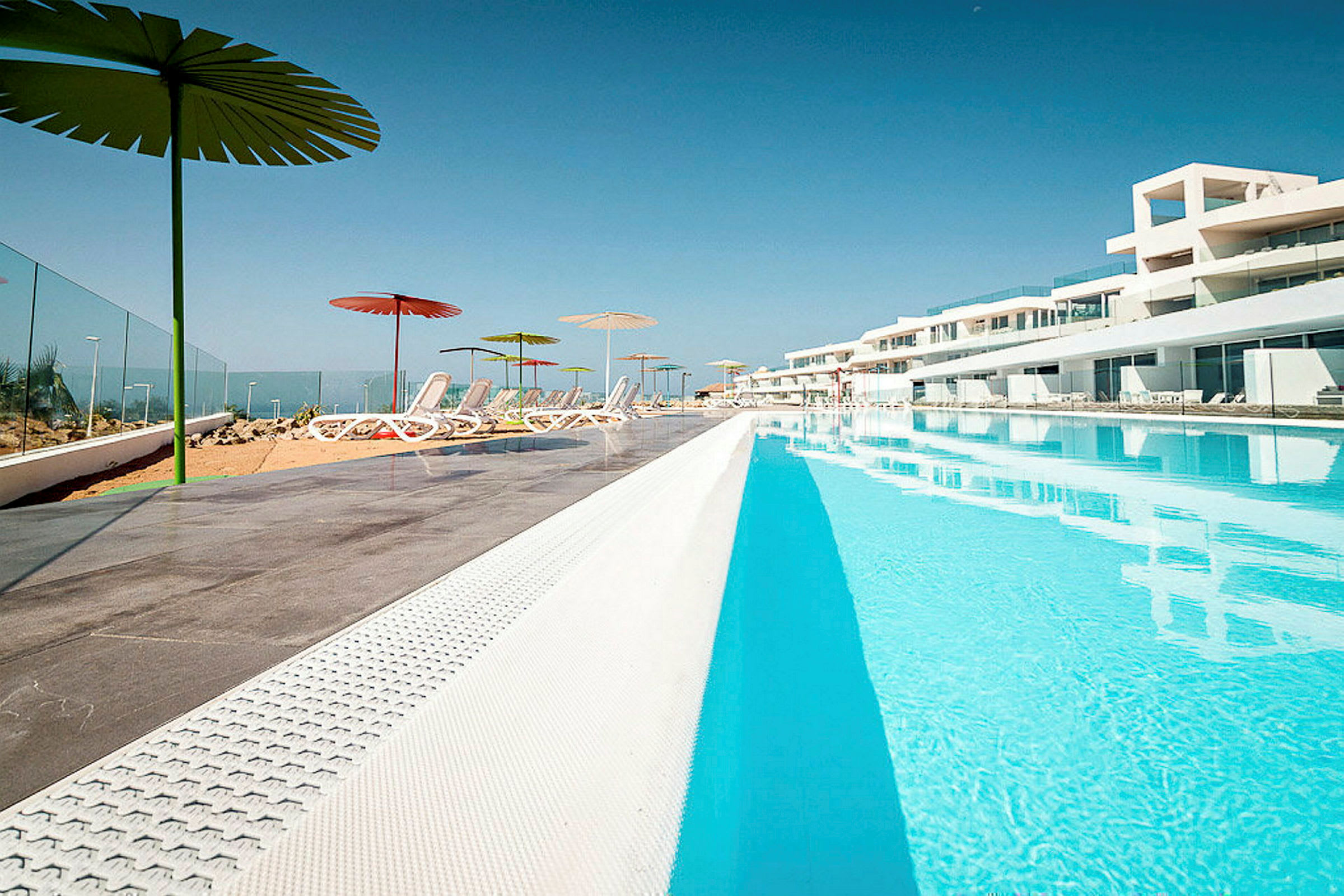 En stor swimmingpool med omkringliggande solstolar och parasoller utomhus. (AI-genererad text)