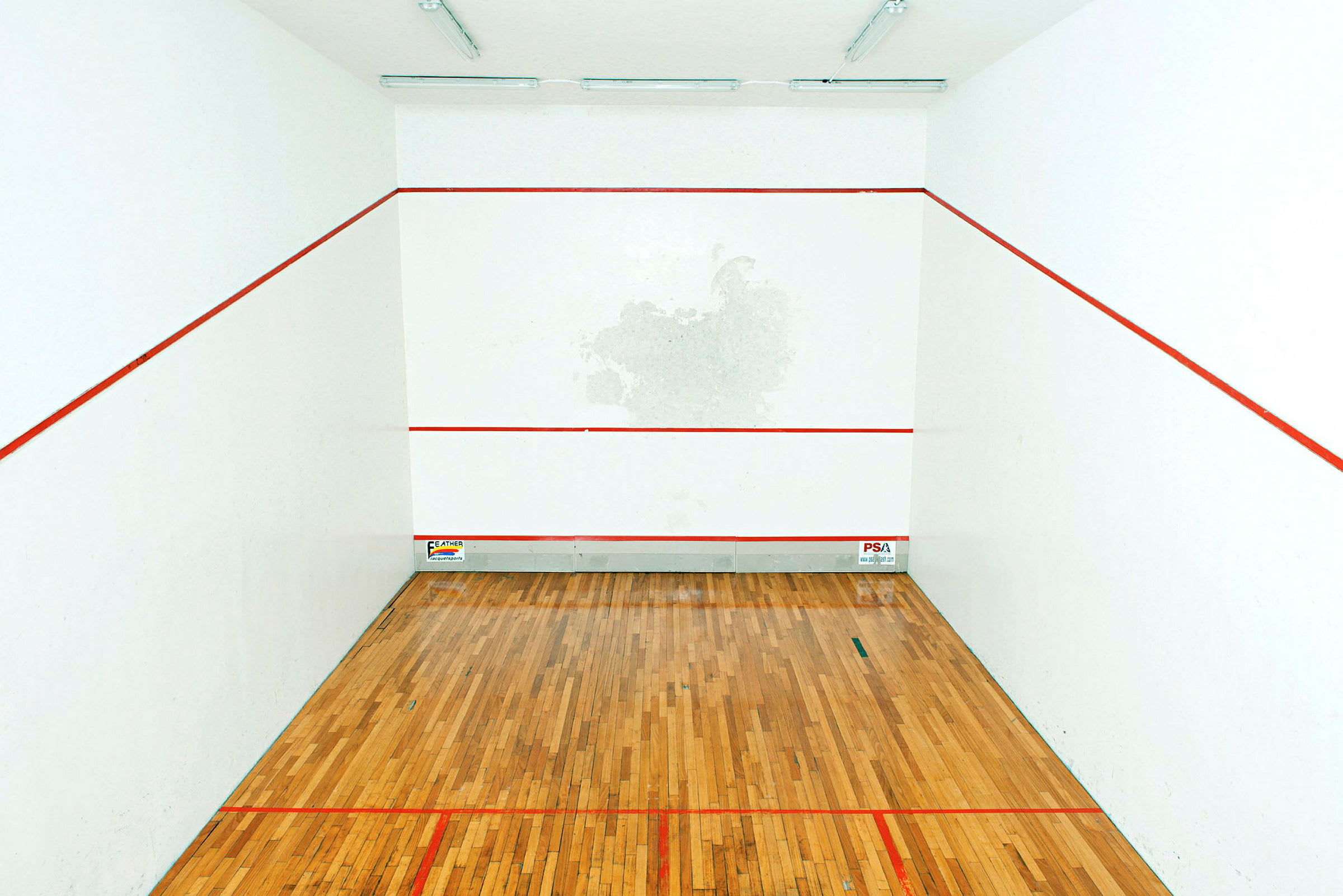 Bild av en squashbana med träparkettgolv och vita väggar markerade med röda linjer. (AI-genererad text)