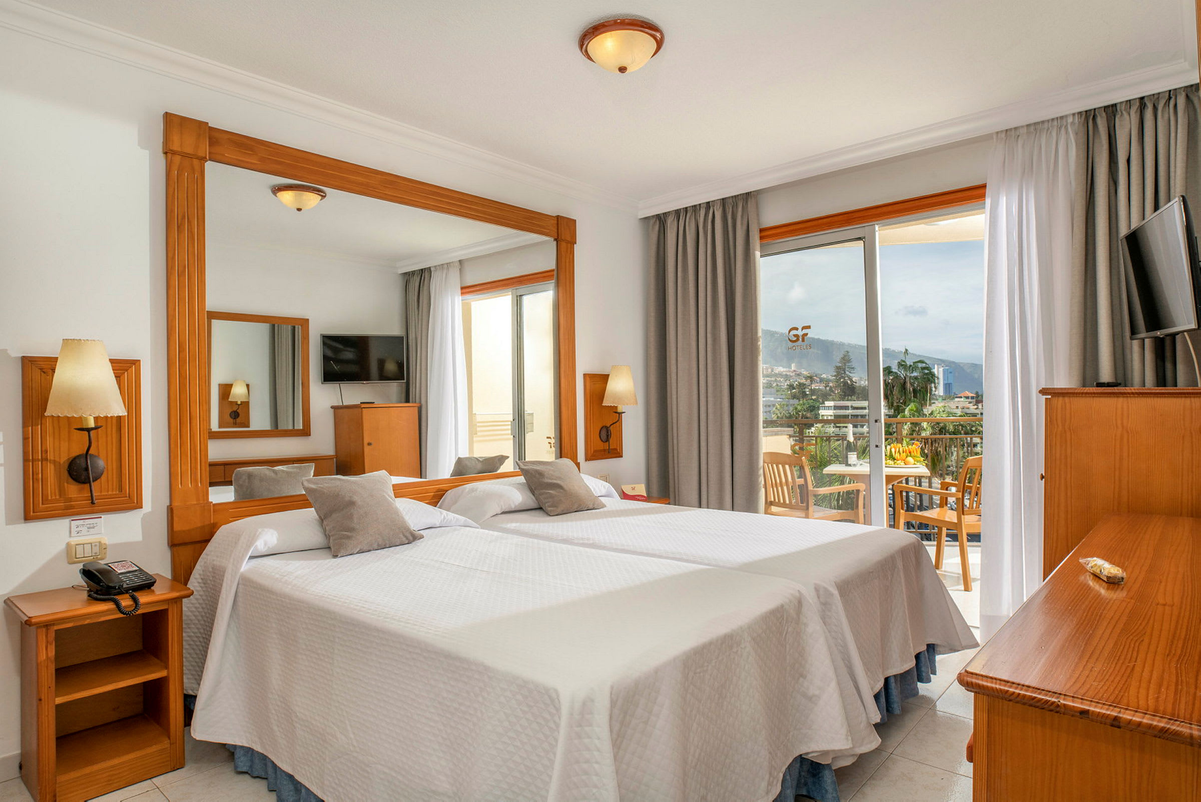 Hotellrum med två enkelsängar, en spegel, en TV och en balkong med sittplats samt utsikt. (AI-genererad text)