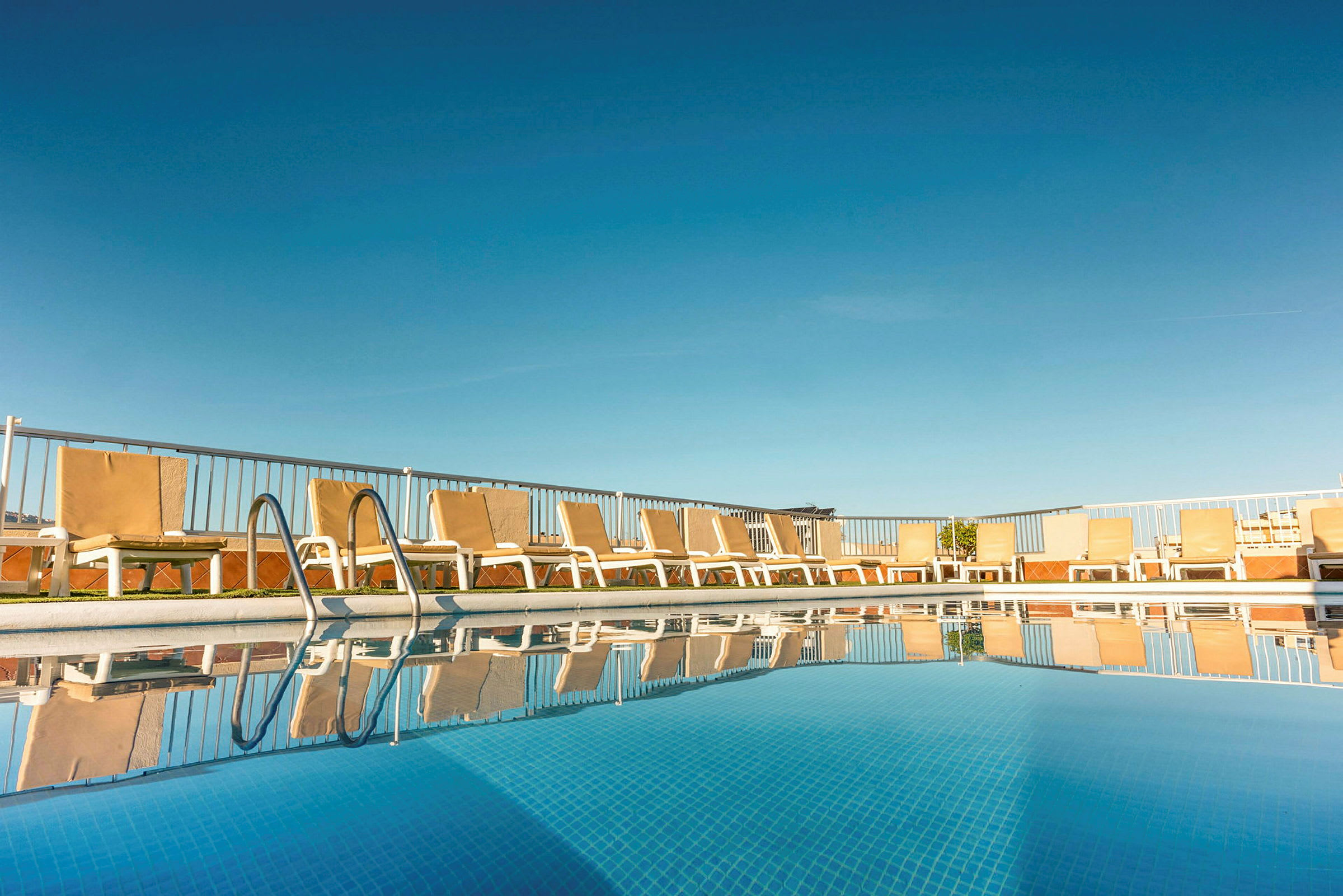 Solstolar och pool på ett hotell med klar blå himmel. (AI-genererad text)