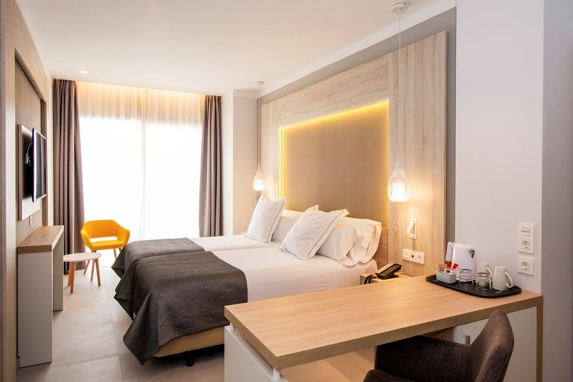 Modernt hotellrum med två enkelsängar, skrivbord och gul stol. (AI-genererad text)