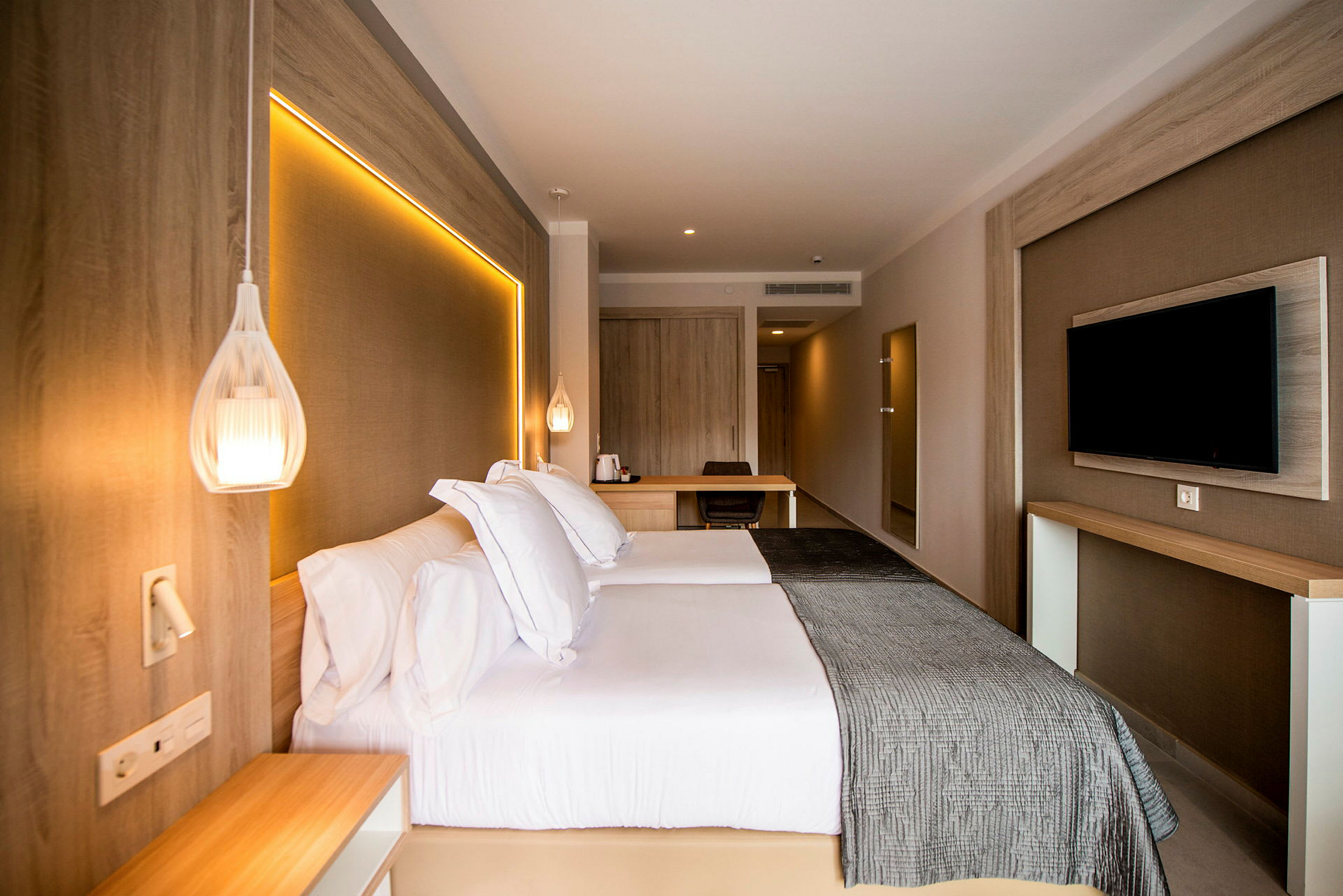 Hotellrum med dubbelsäng, väggmonterad TV och skrivbord. (AI-genererad text)