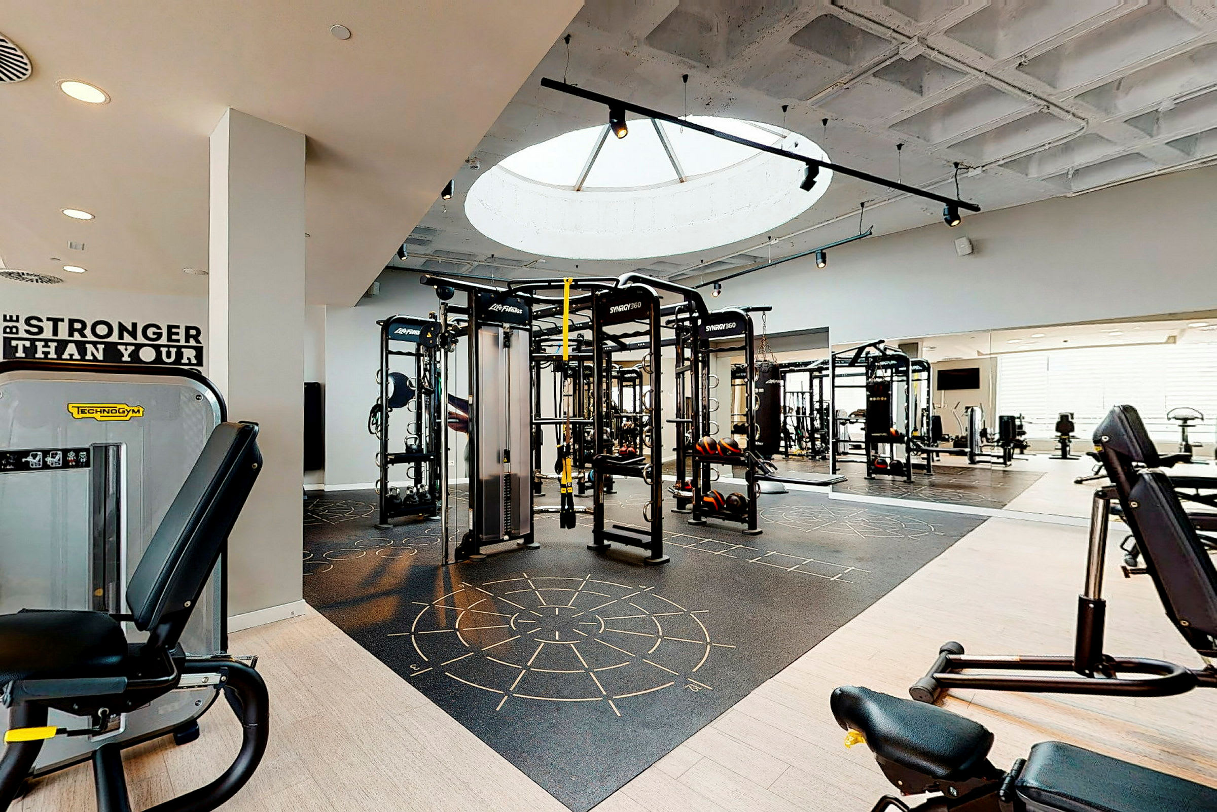 Ett modernt gym med träningsmaskiner och fria vikter, samt ett takfönster som släpper in dagsljus. (AI-genererad text)