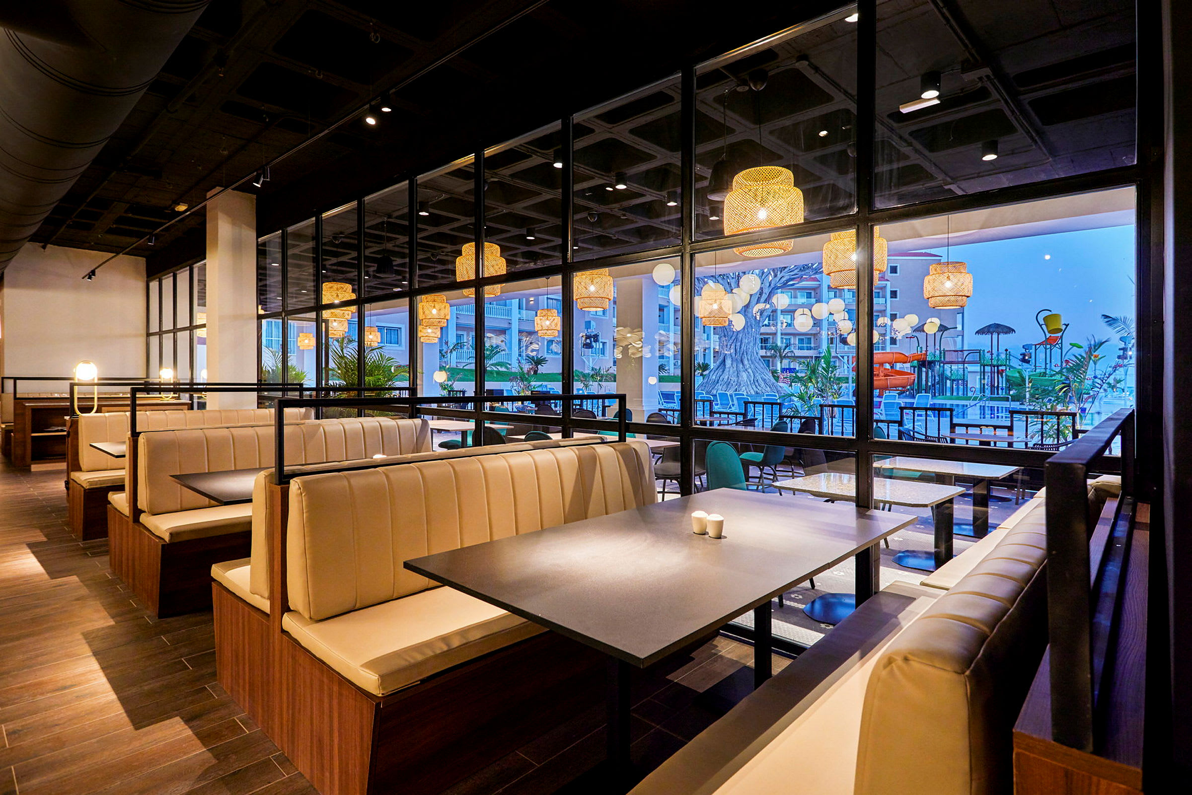 En modern restaurang med ljusa bås och stora fönster som vetter mot en uteplats med pool och dekorationer. (AI-genererad text)