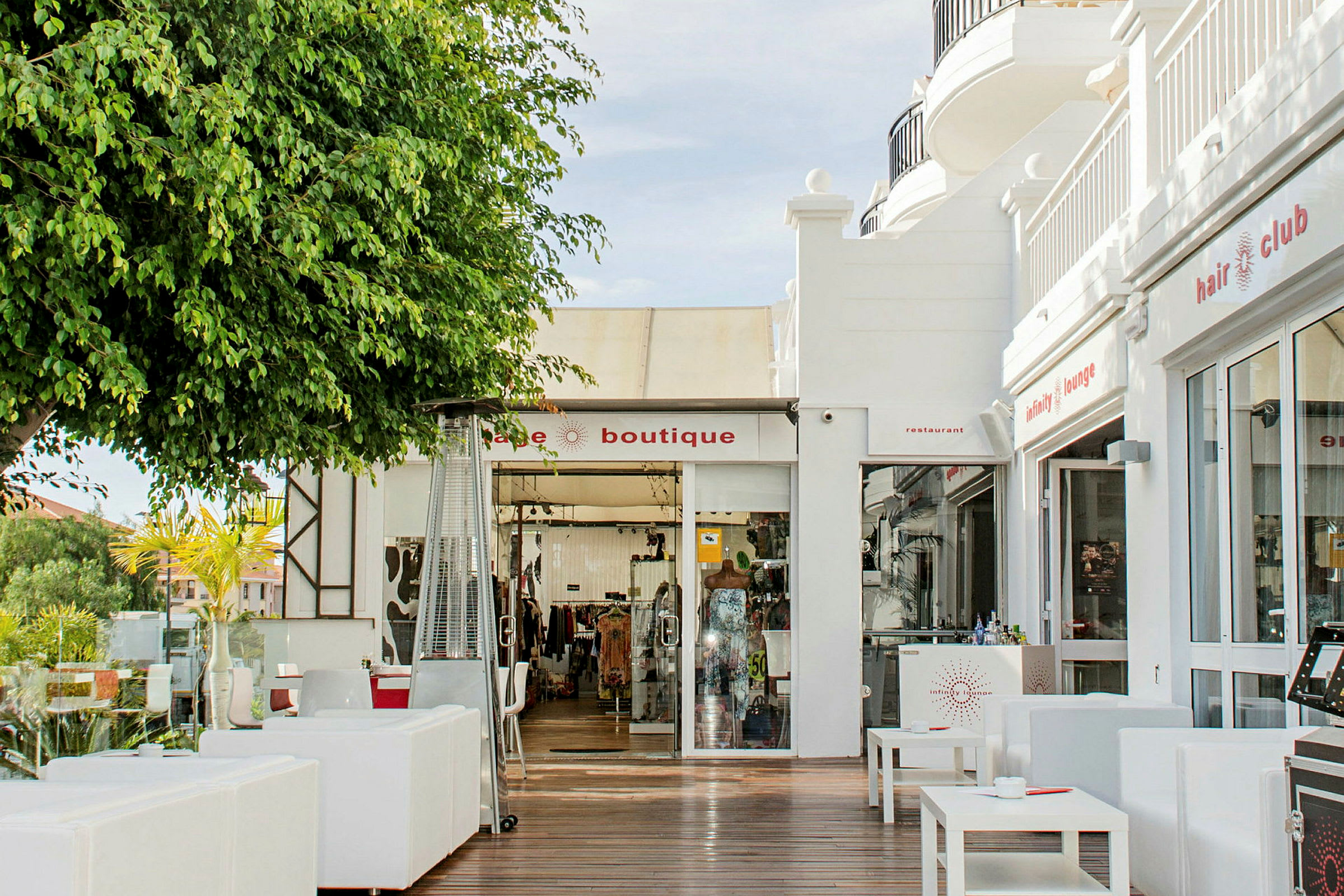 Bild av en butik och restaurang med utomhusmöbler i en solig miljö. (AI-genererad text)