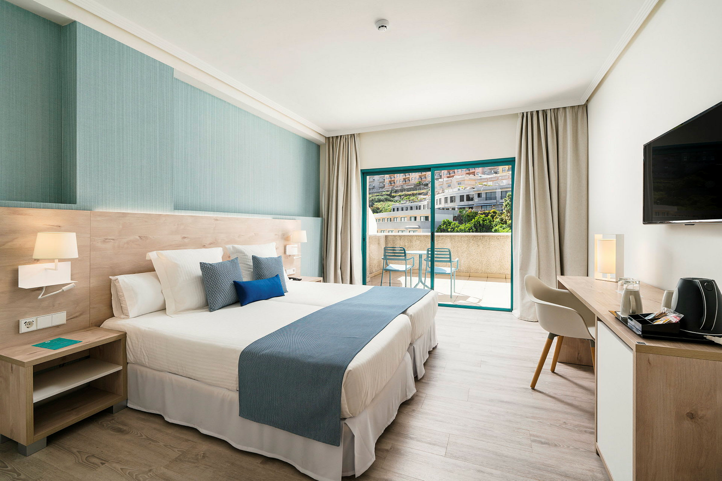 Ett hotellrum med en stor säng, modern inredning, ett skrivbord och stora skjutdörrar som leder till en balkong. (AI-genererad text)