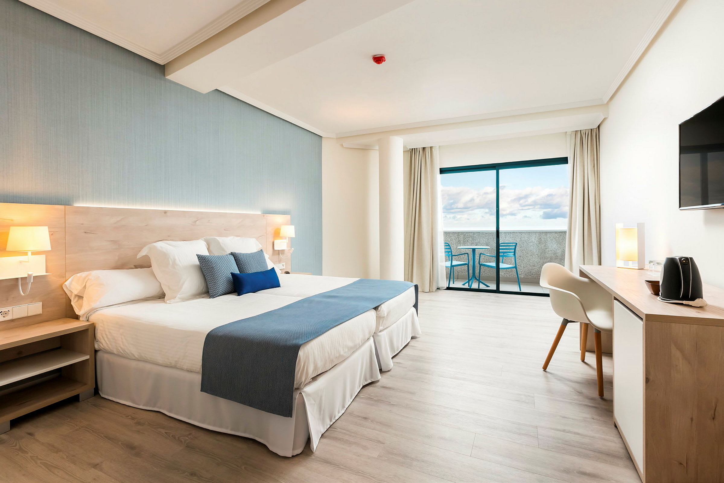 Ljust och modernt hotellrum med dubbelsäng, skrivbord och balkong med utsikt. (AI-genererad text)