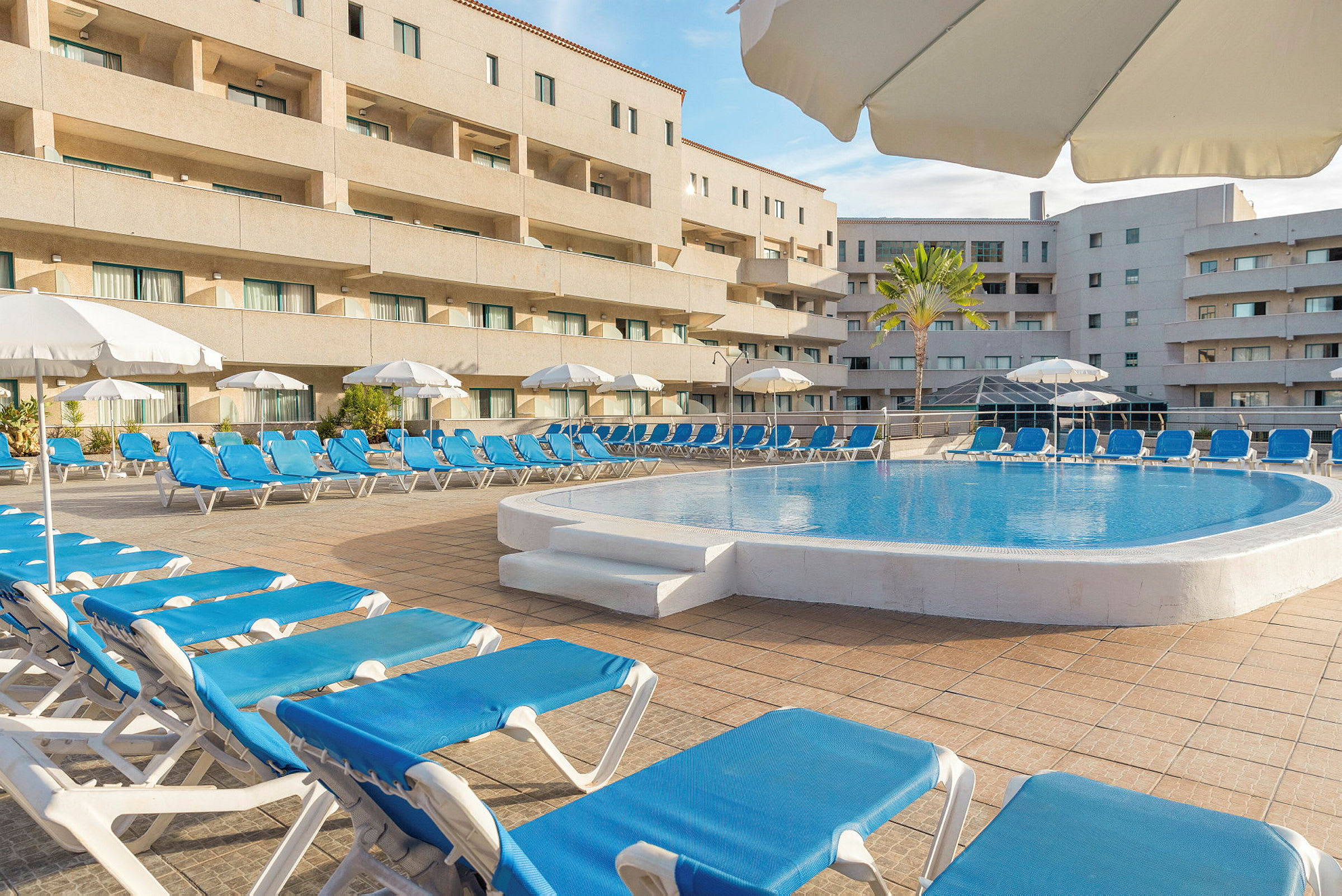 En simbassäng omgiven av blå solstolar och vita parasoller på en hotellterrass. (AI-genererad text)