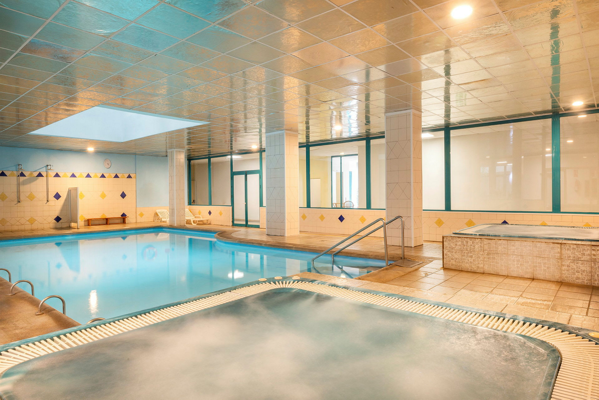 En inomhuspool med ett angränsande bubbelbad i ett ljust utrymme. (AI-genererad text)