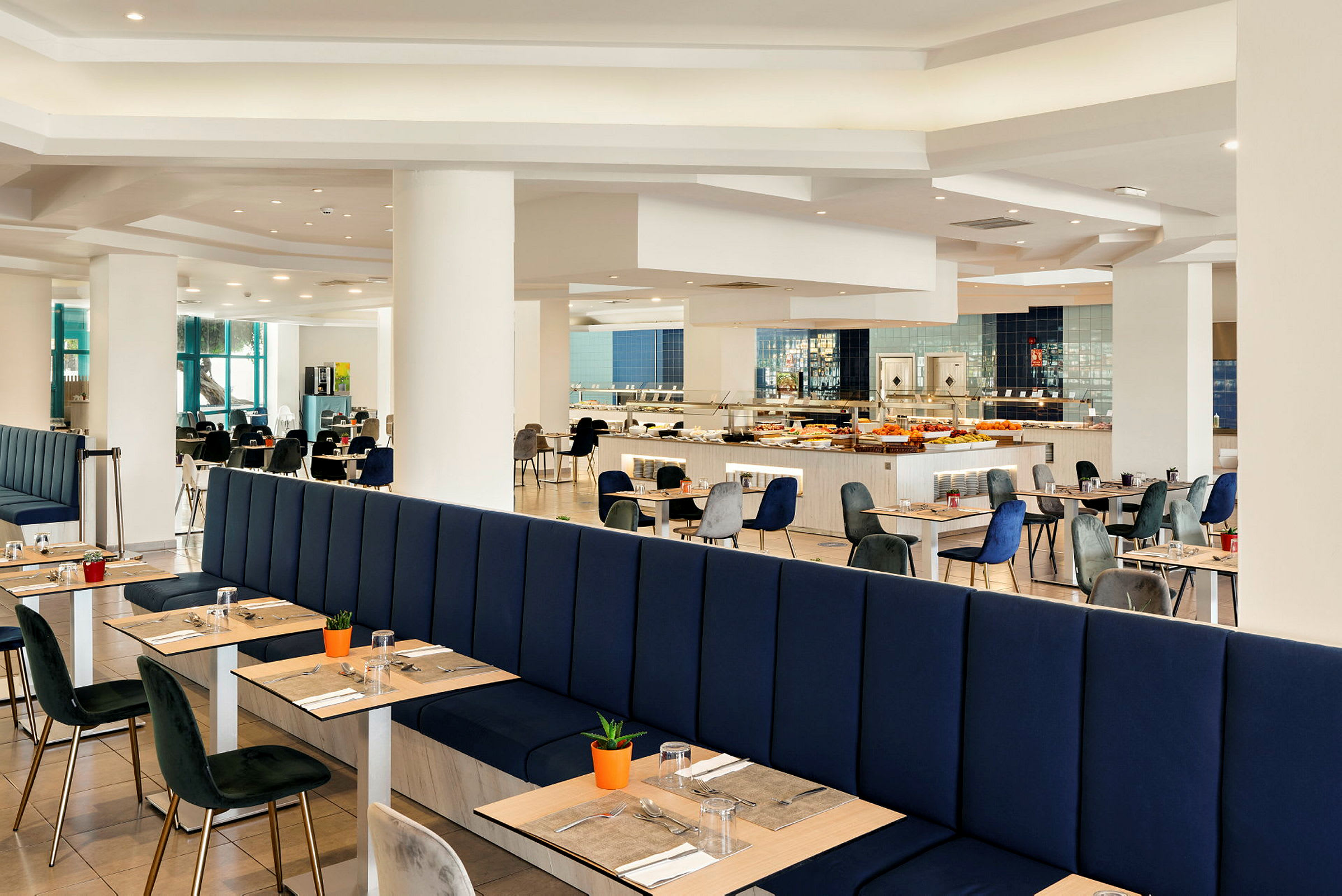 En rymlig restaurang med blå stoppade bås och träbord, omgiven av moderna stolar och bufféområden. (AI-genererad text)