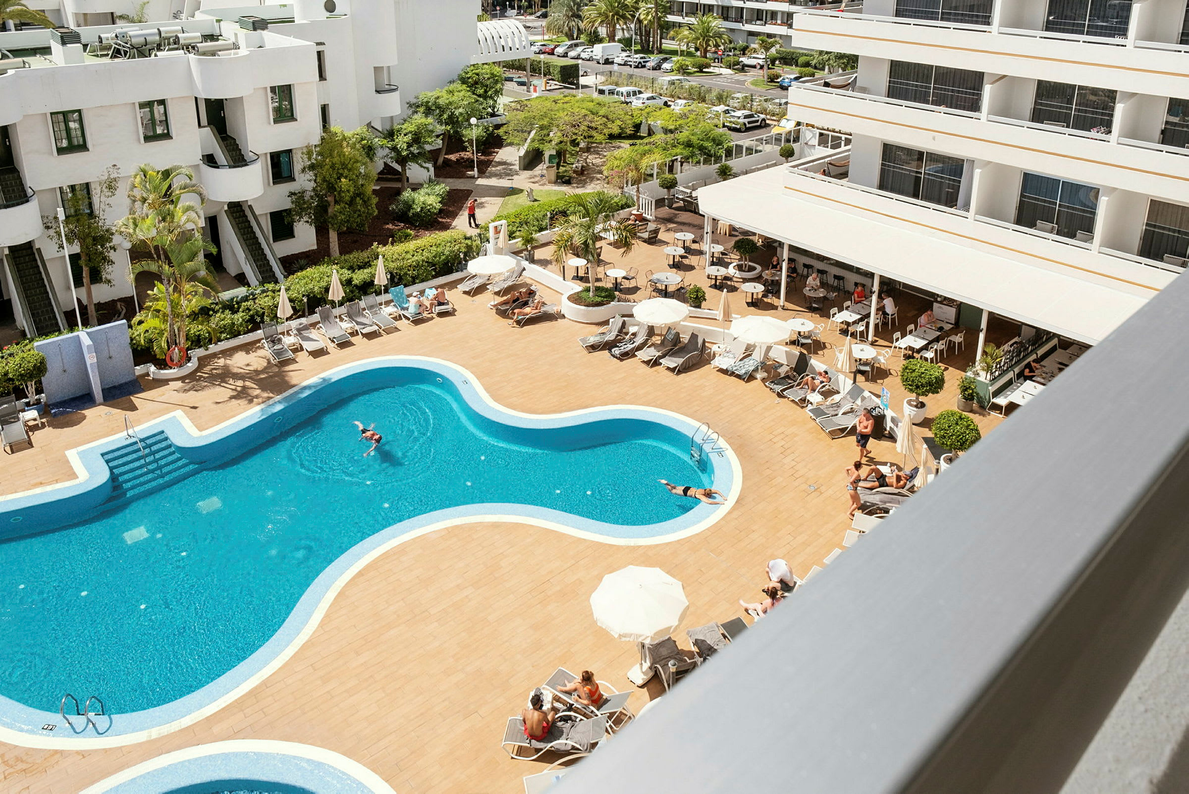 Bild av en hotellpool med solstolar och parasoller, omgiven av hotellbyggnader. (AI-genererad text)