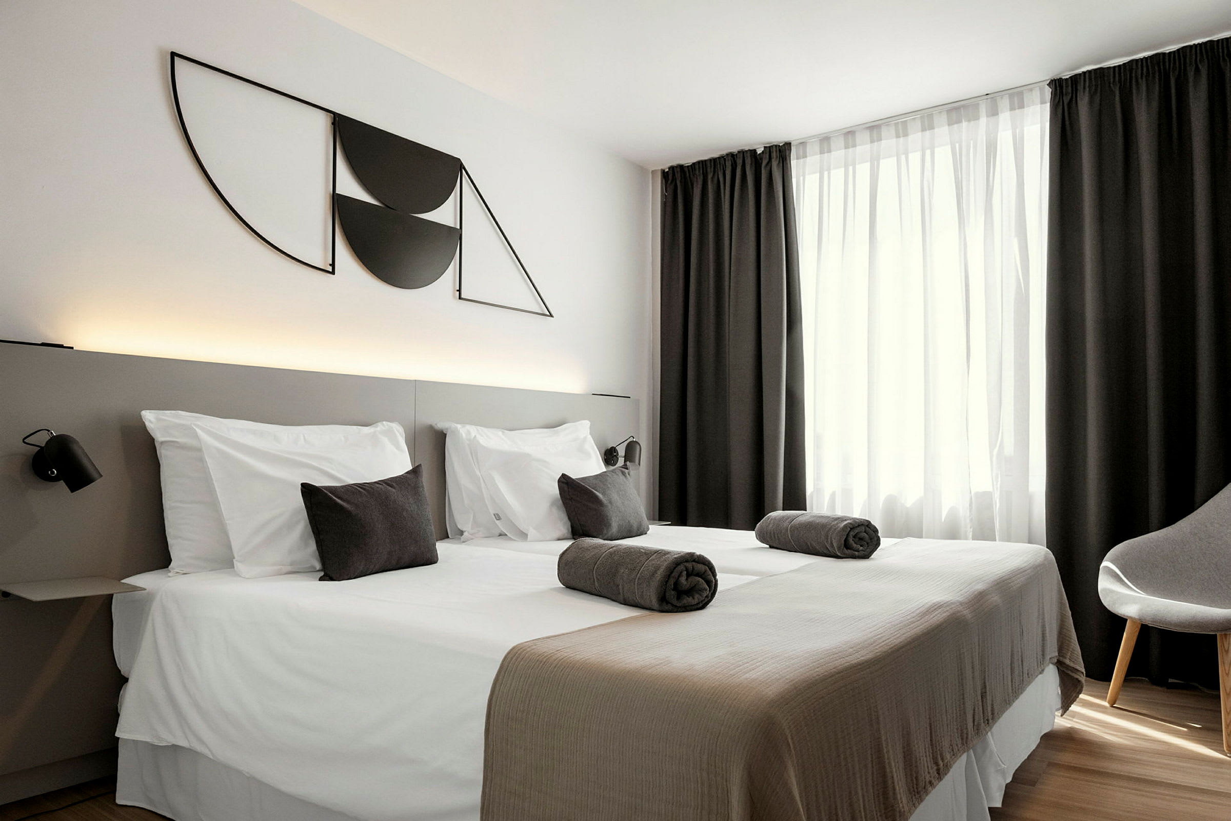 Ett hotellrum med två enkelsängar, mörka gardiner och modernt väggdekor. (AI-genererad text)