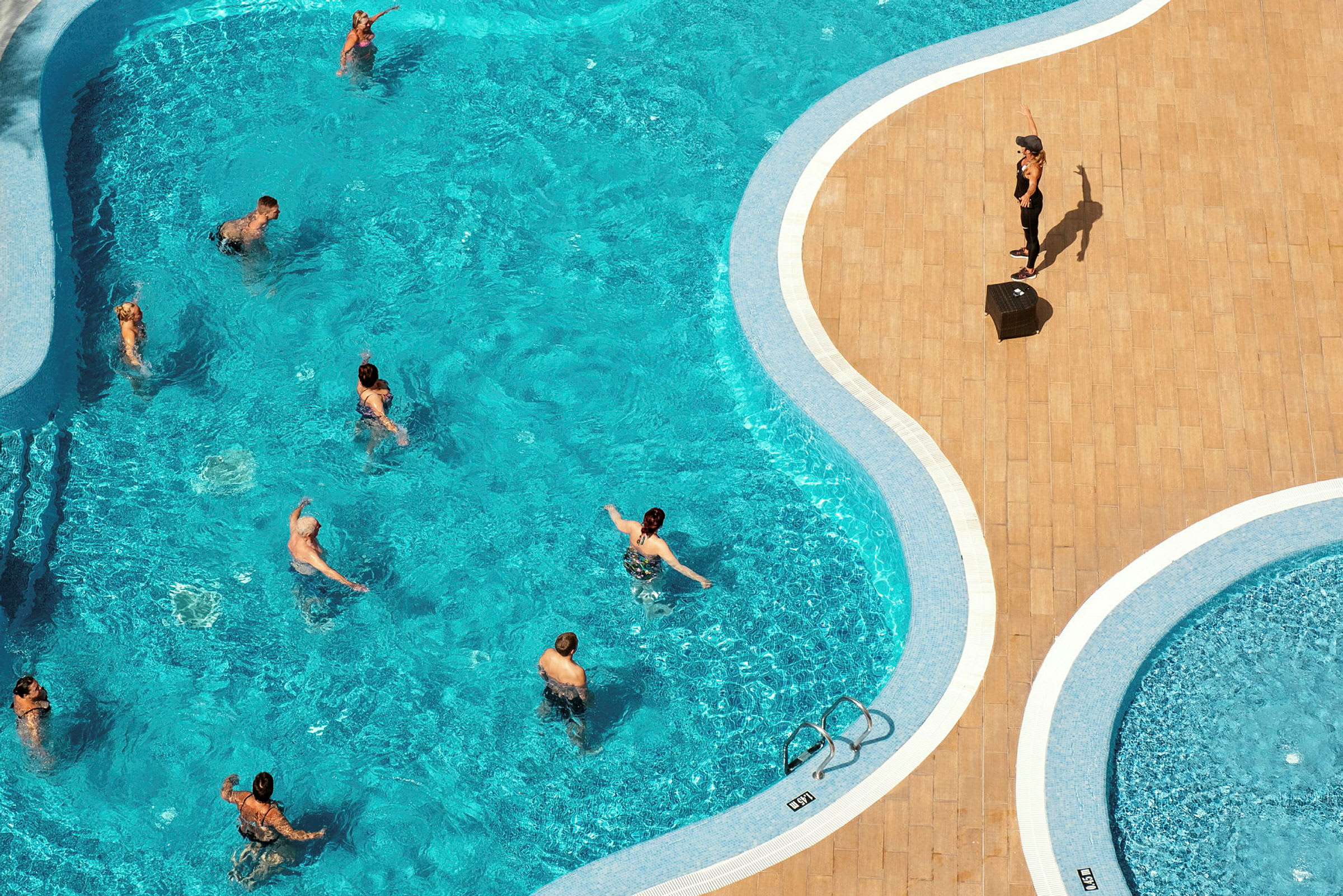 En pool med människor som tränar aqua aerobics under ledning av en instruktör. (AI-genererad text)