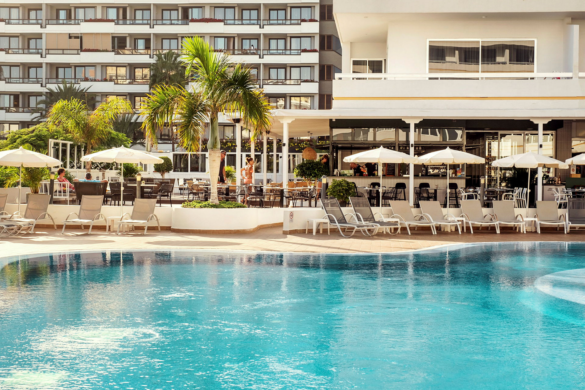 Bild av en hotellpool i närheten av ett område med solstolar och parasoller. (AI-genererad text)