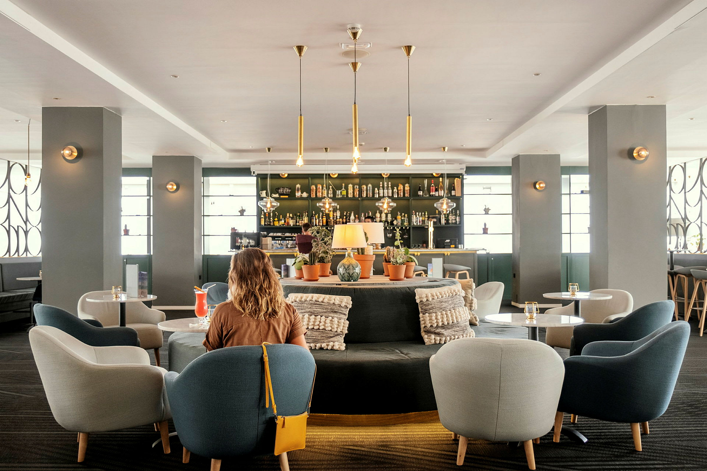 Interiör av ett modernt hotellbarområde med sittplatser och dekorationer. En kvinna med rygg mot kameran i förgrunden. (AI-genererad text)
