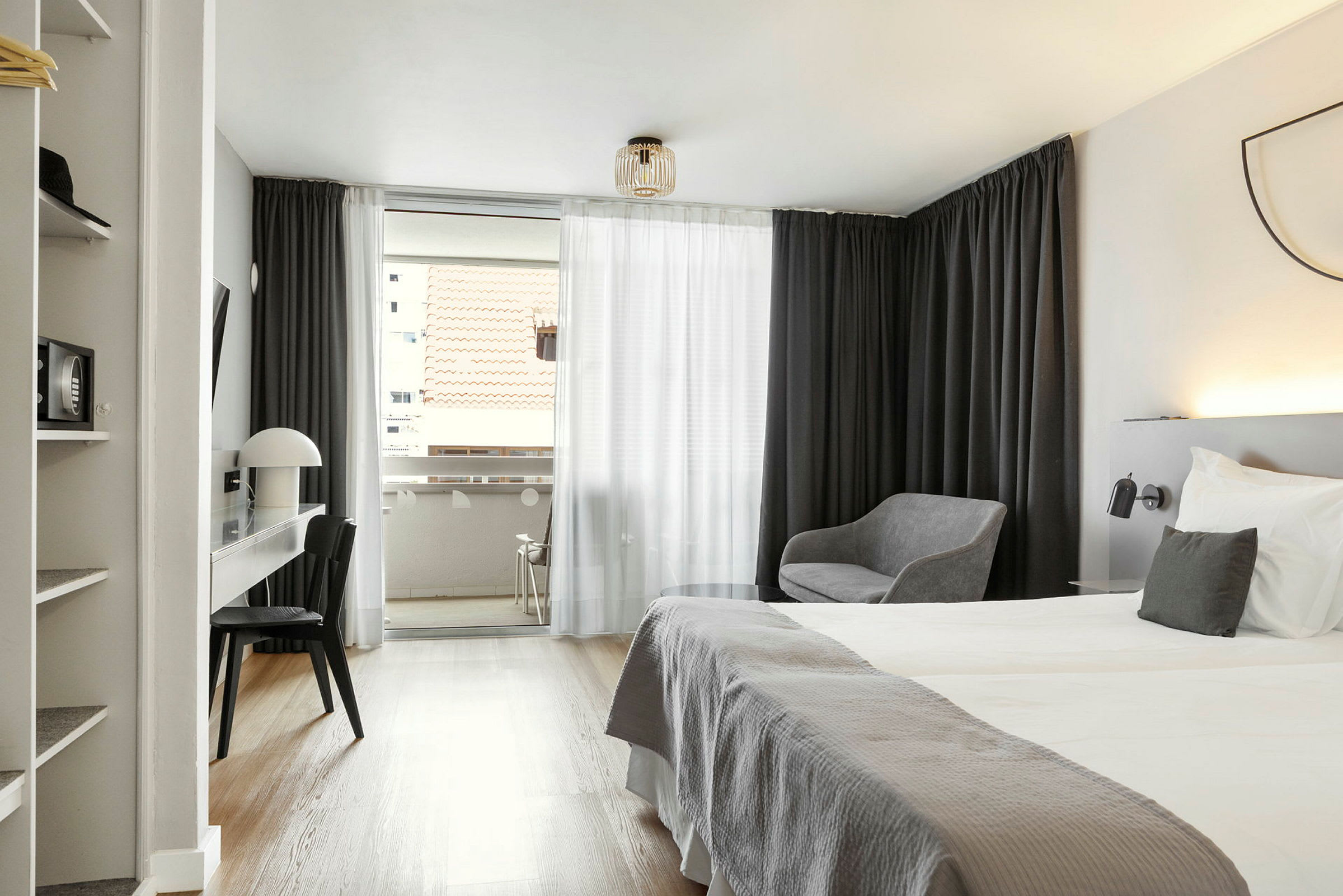 Ett hotellrum med dubbelsäng, skrivbord, stol och sittgrupp; utsikt mot en balkong med takutsikt. (AI-genererad text)