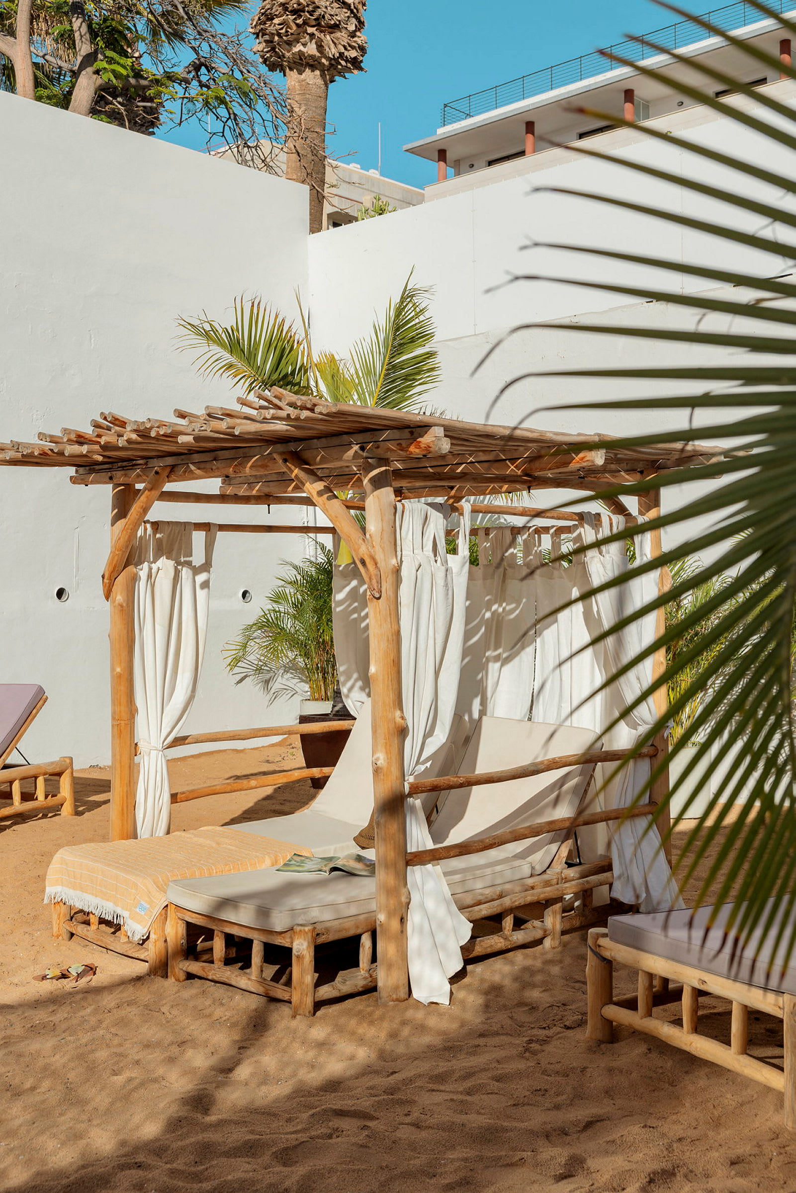 Träpergola med vita gardiner och solstolar på sand. (AI-genererad text)