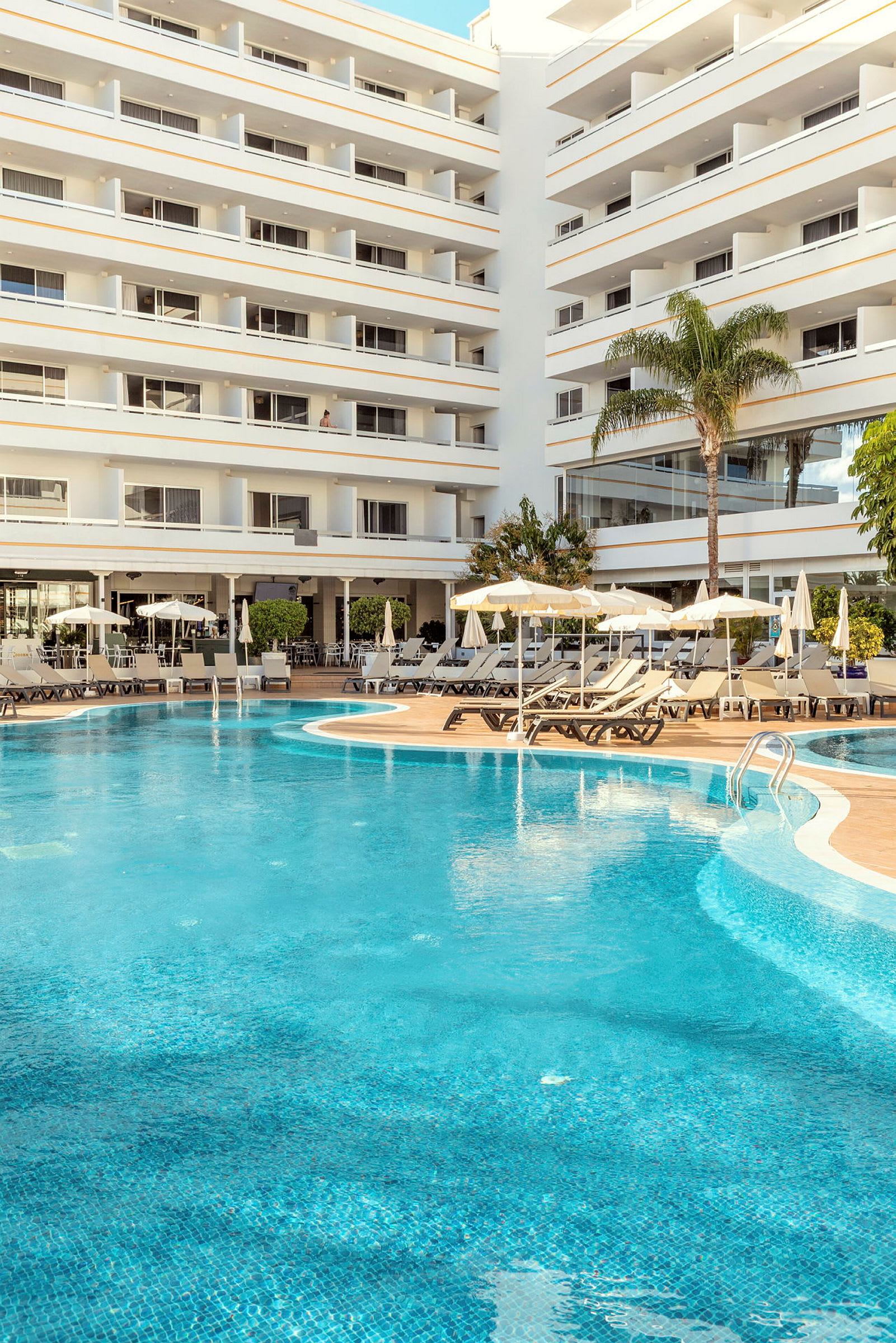 Poolområde framför ett fler våningar högt hotell. (AI-genererad text)