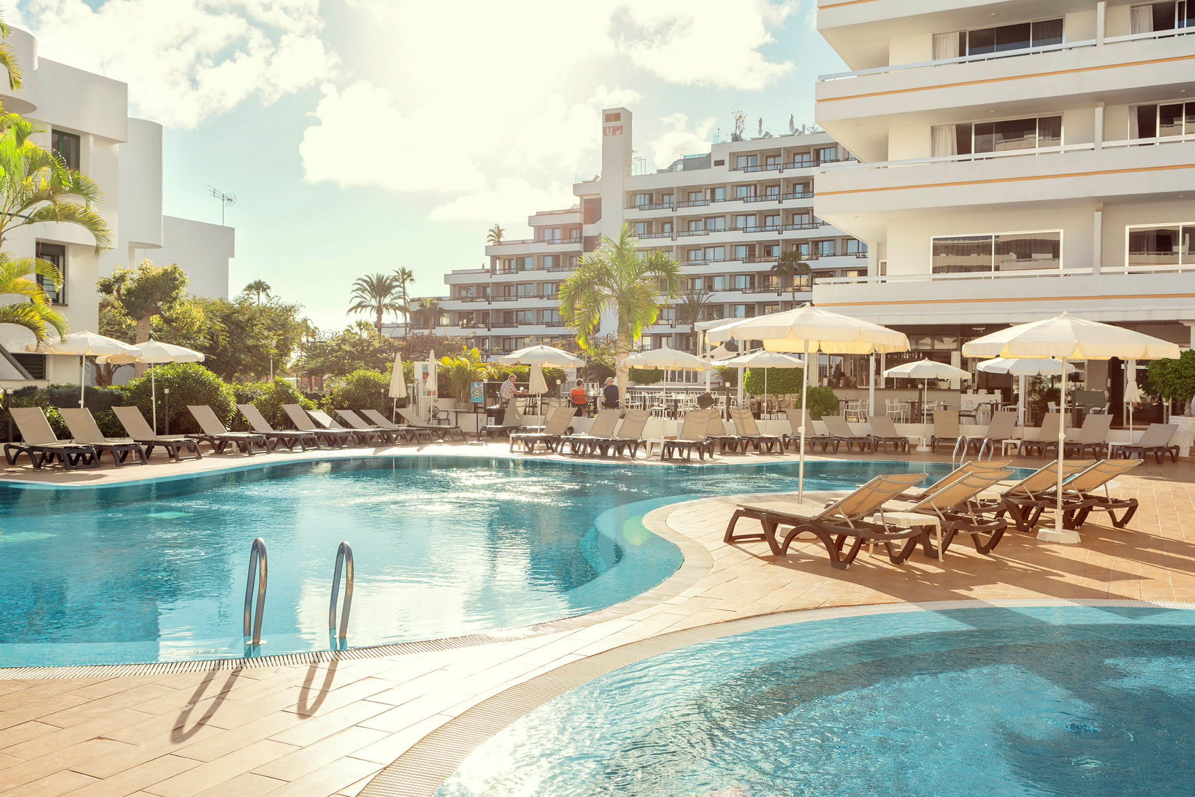 Hotellpool med solstolar och parasoller, omgivet av byggnader. (AI-genererad text)
