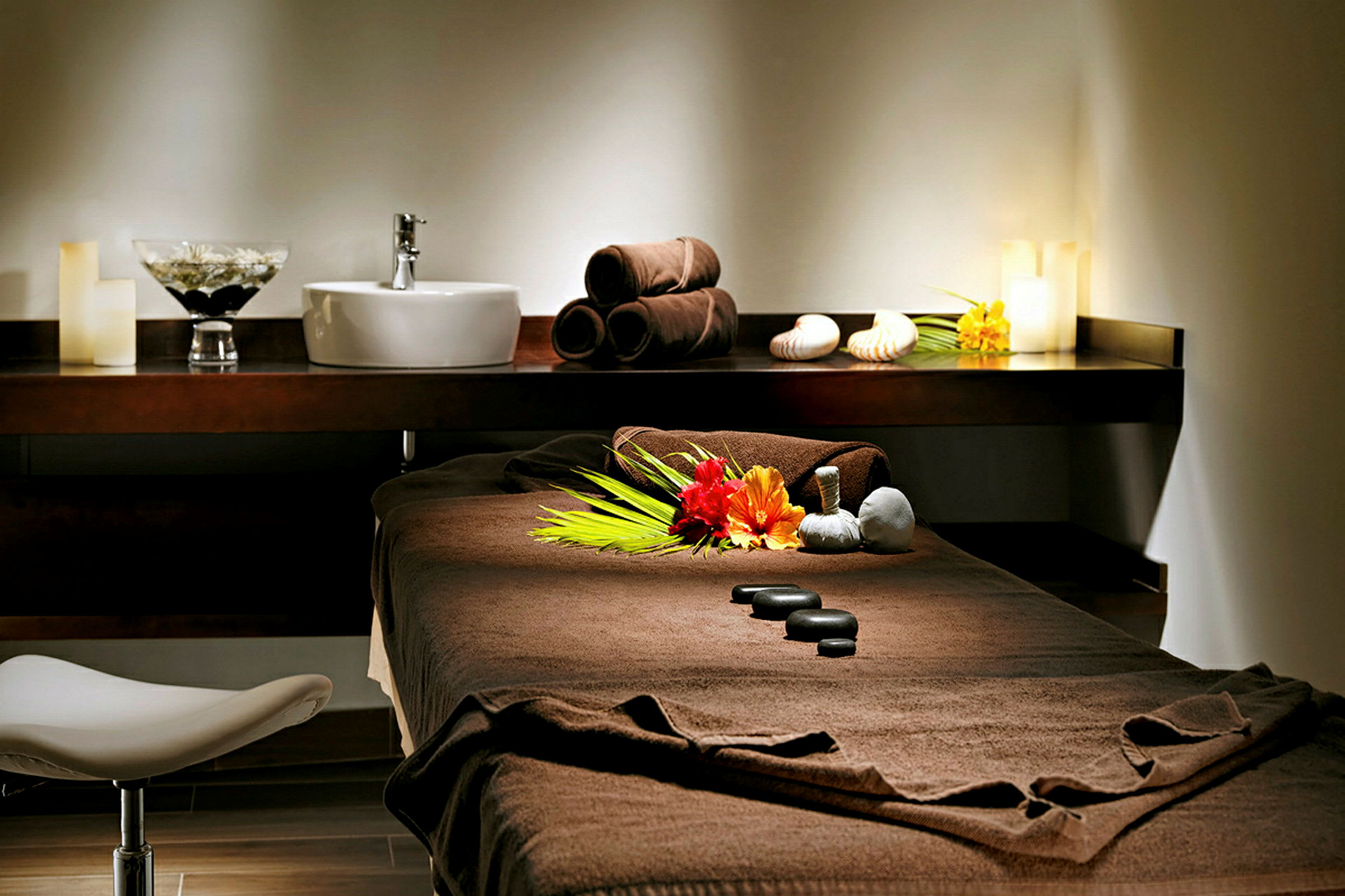 En massagesäng i ett upplyst rum med dekorativa stenar och blommor. (AI-genererad text)